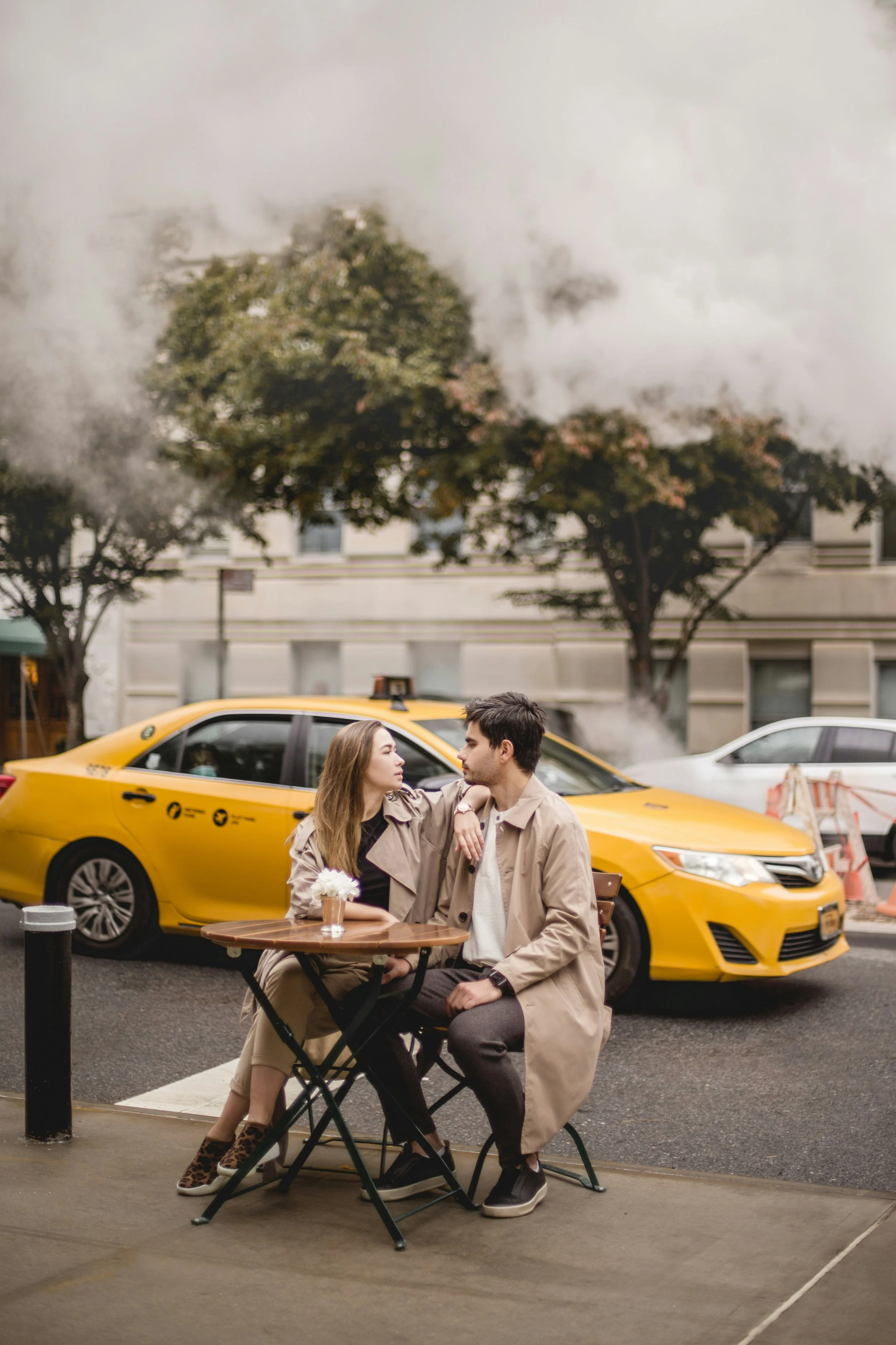 Couple sits at a table on the street in front of a yellow cab