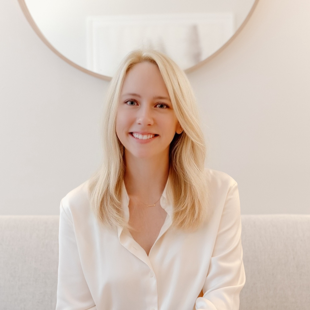 blonde smiling woman sitting on a couch with mirror behind her