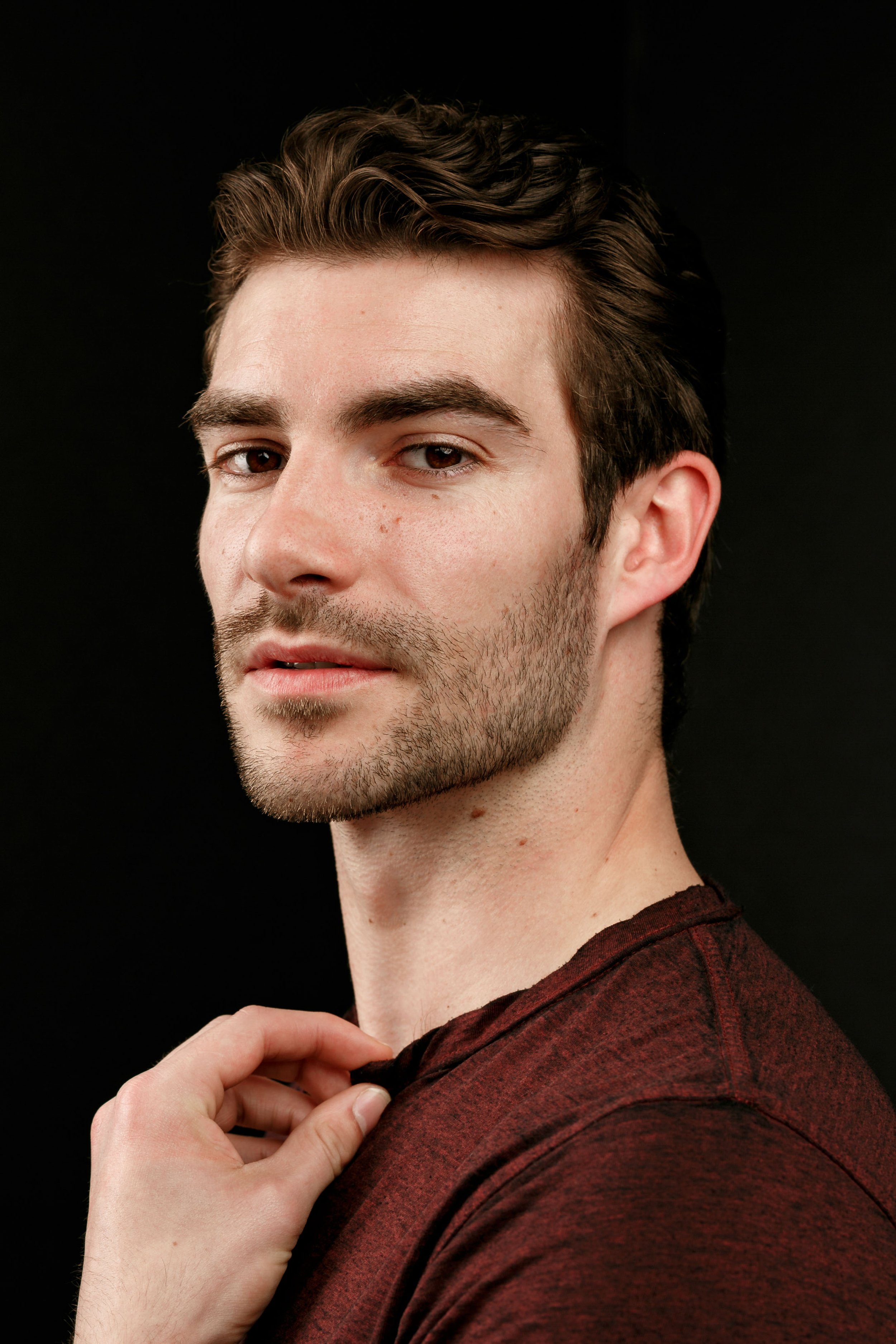 very fit male model in dark red shirt posing for a candid moment in front of black background