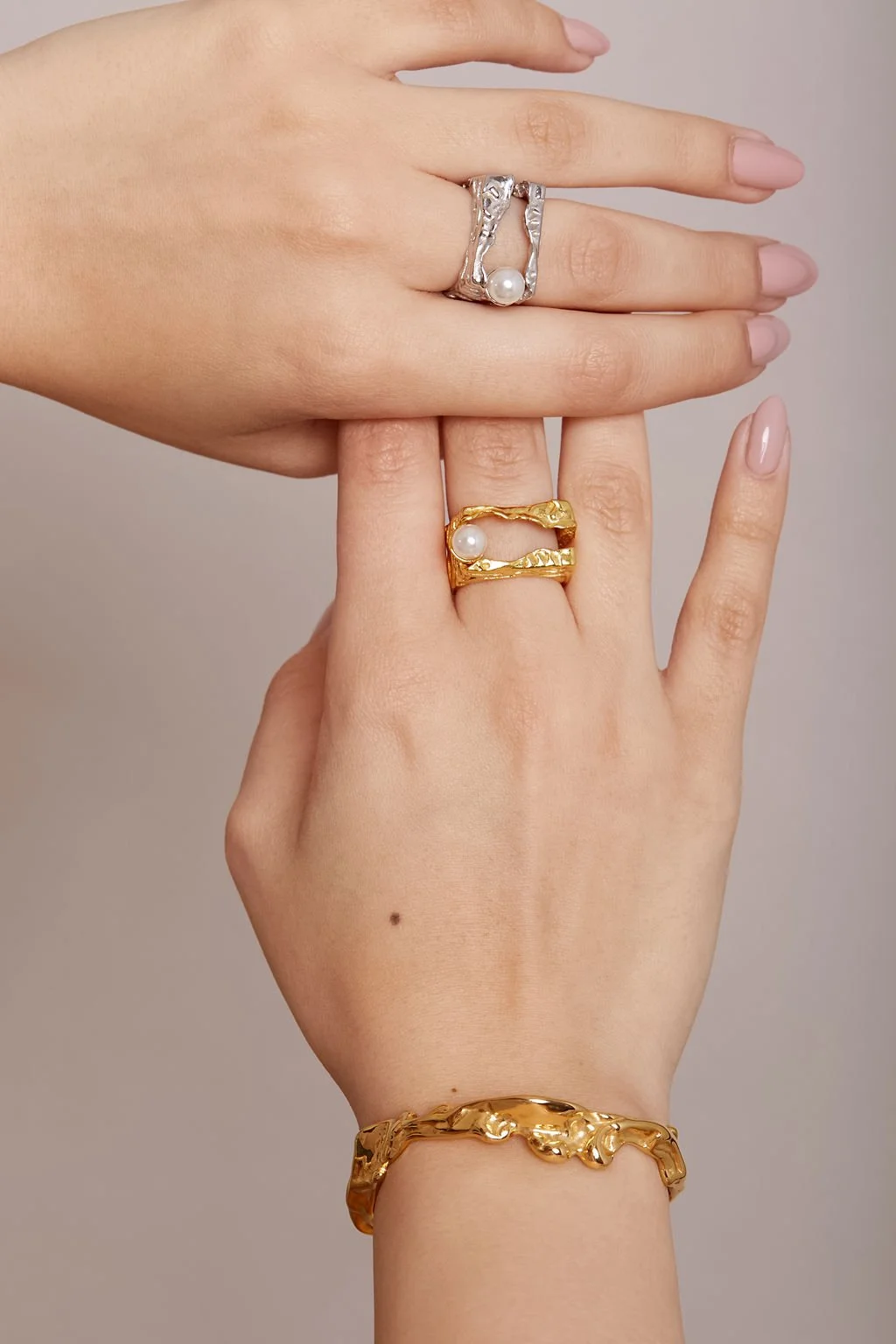 hand studio shot of organic shaped gold and silver ring with pearl and gold bracelet in natural light