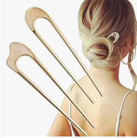 A woman with blonde hair styled in a bun holding two large tuning forks against her shoulder.