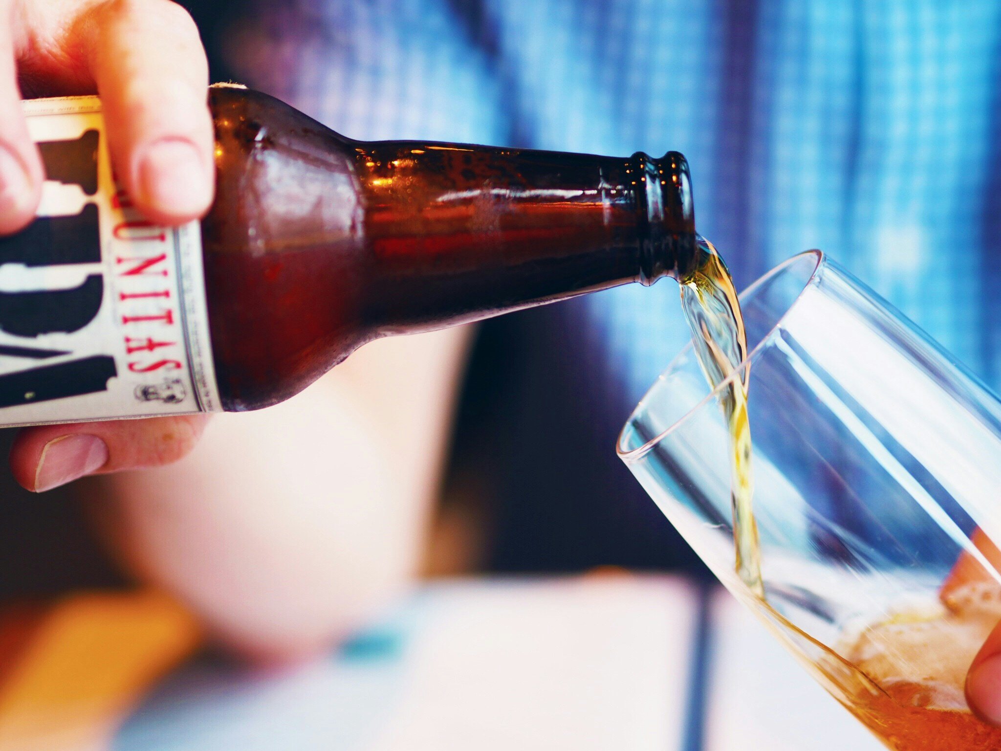 A person pouring beer from a brown bottle into a clear glass.