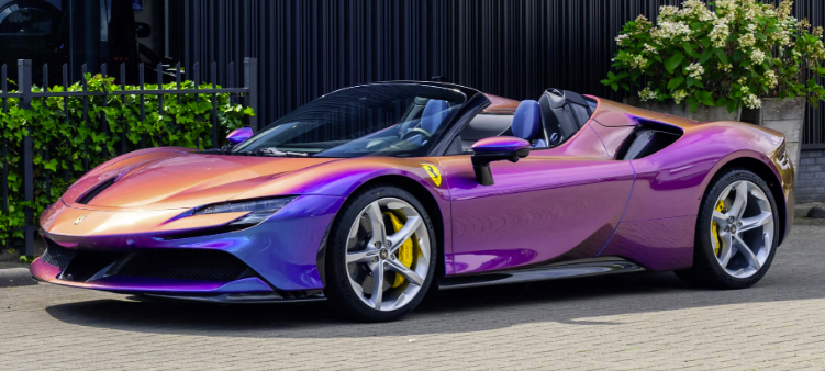 A colorful Ferrari convertible sports car parked outdoors with plants and a building in the background.