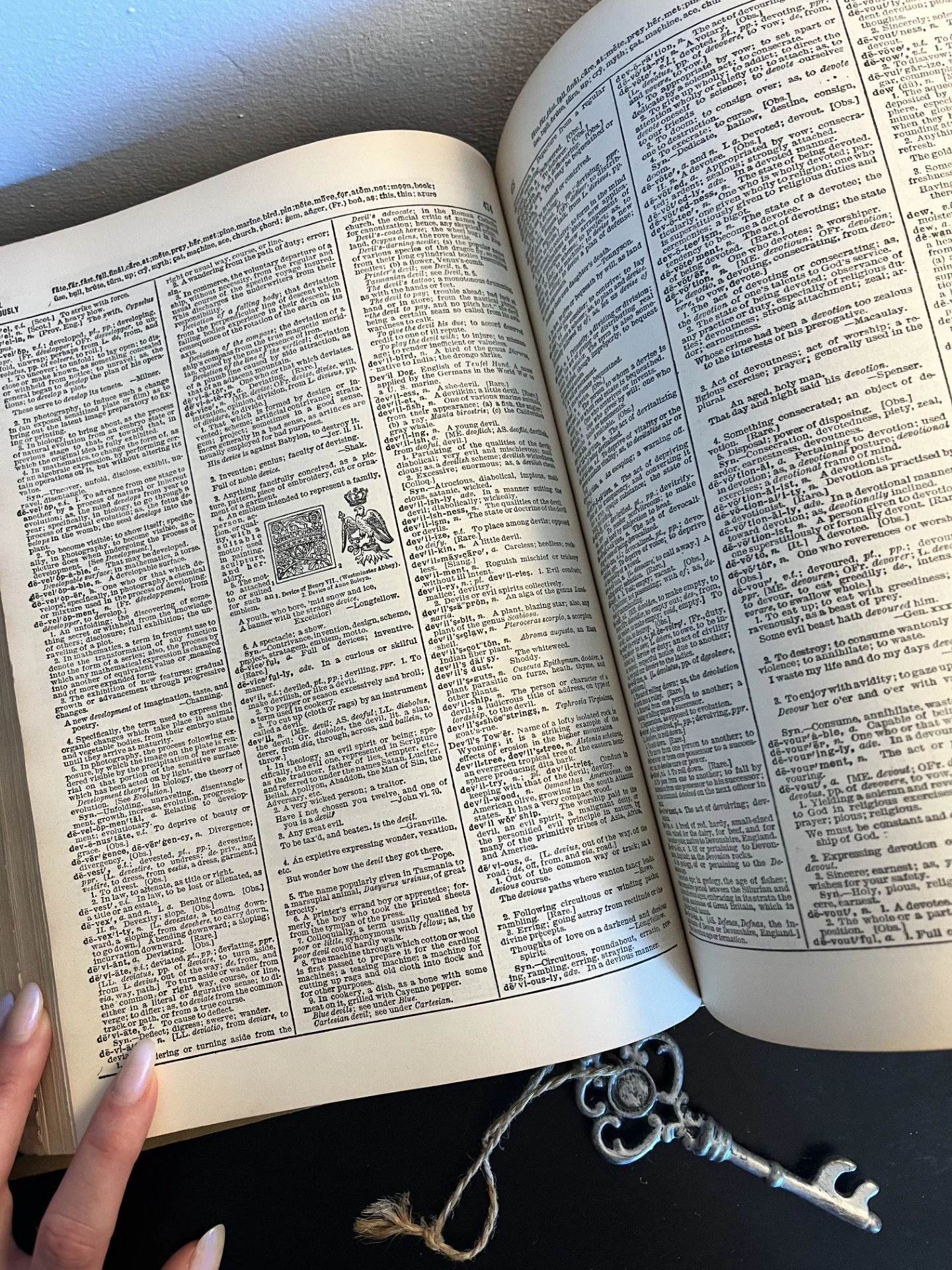 Open Bible with small illustration, Bible key at bottom, hand holding page, gray wall in background.