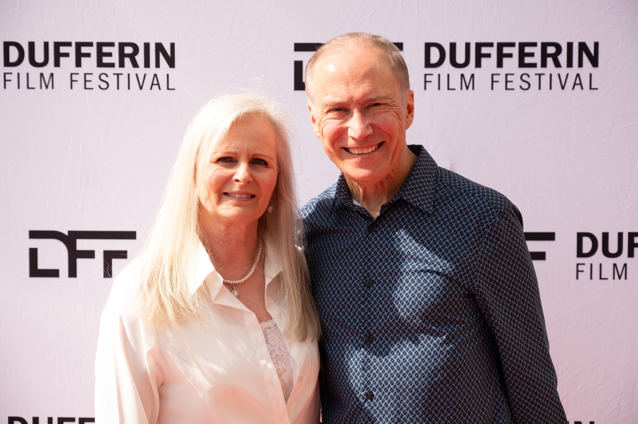 Two people smiling at Dufferin Film Festival event, standing in front of a branded backdrop.