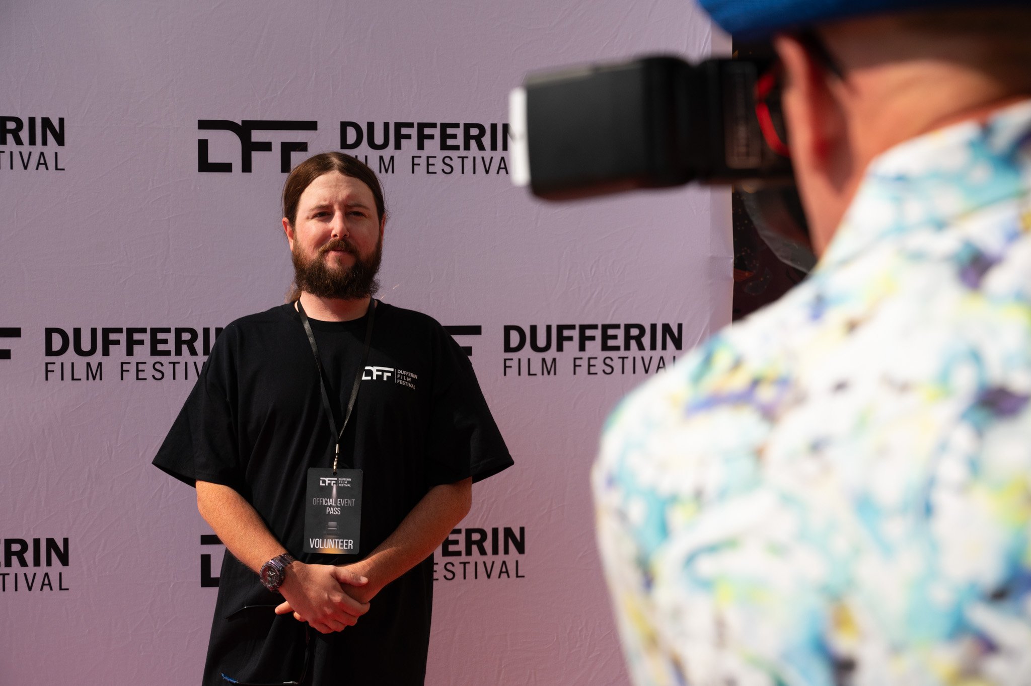 Man posing at Dufferin Film Festival with volunteer badge, facing camera.