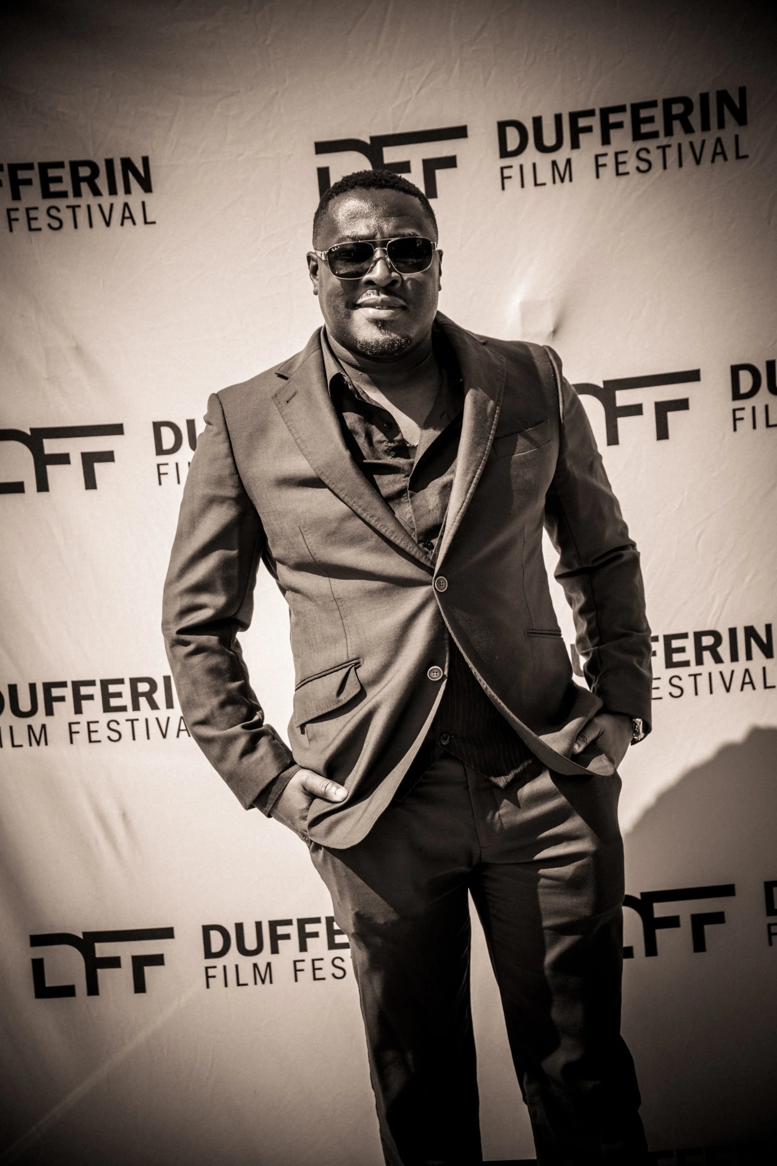 Person in sunglasses and suit at Dufferin Film Festival red carpet event with logo backdrop
