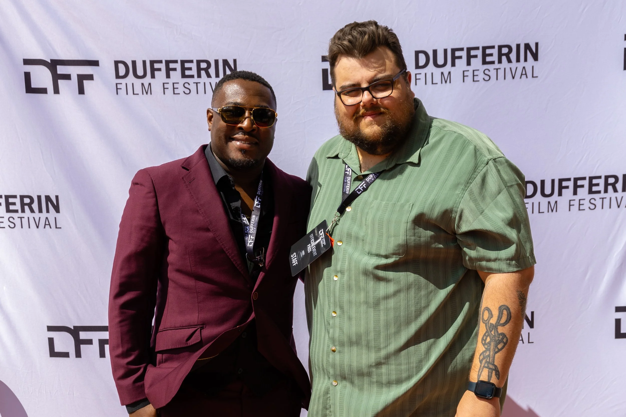 Two men standing in front of a Dufferin Film Festival backdrop, wearing suits and festival badges.