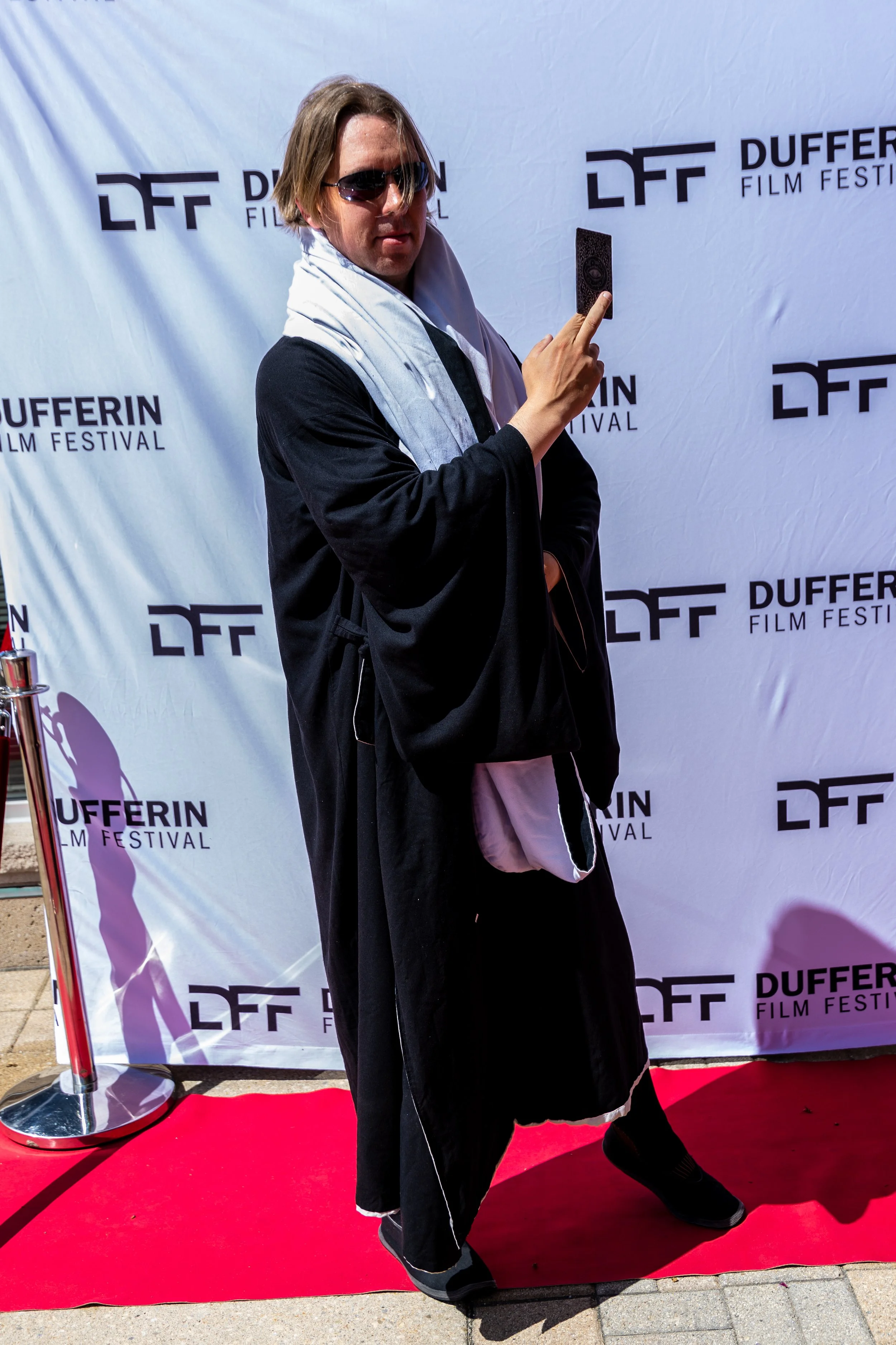 Person in black robe and sunglasses posing on a red carpet at Dufferin Film Festival.