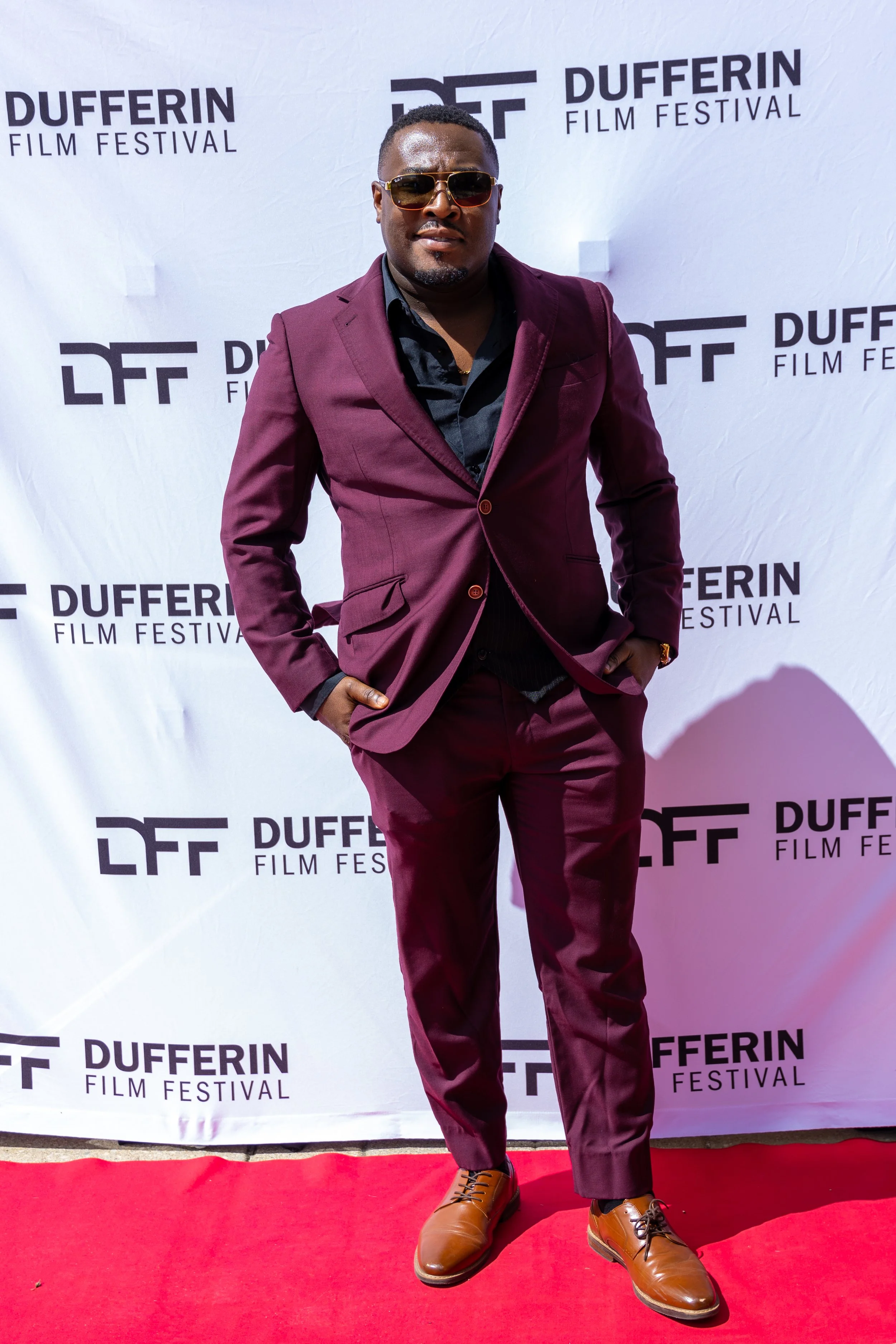 Man in burgundy suit and sunglasses on red carpet at Dufferin Film Festival.