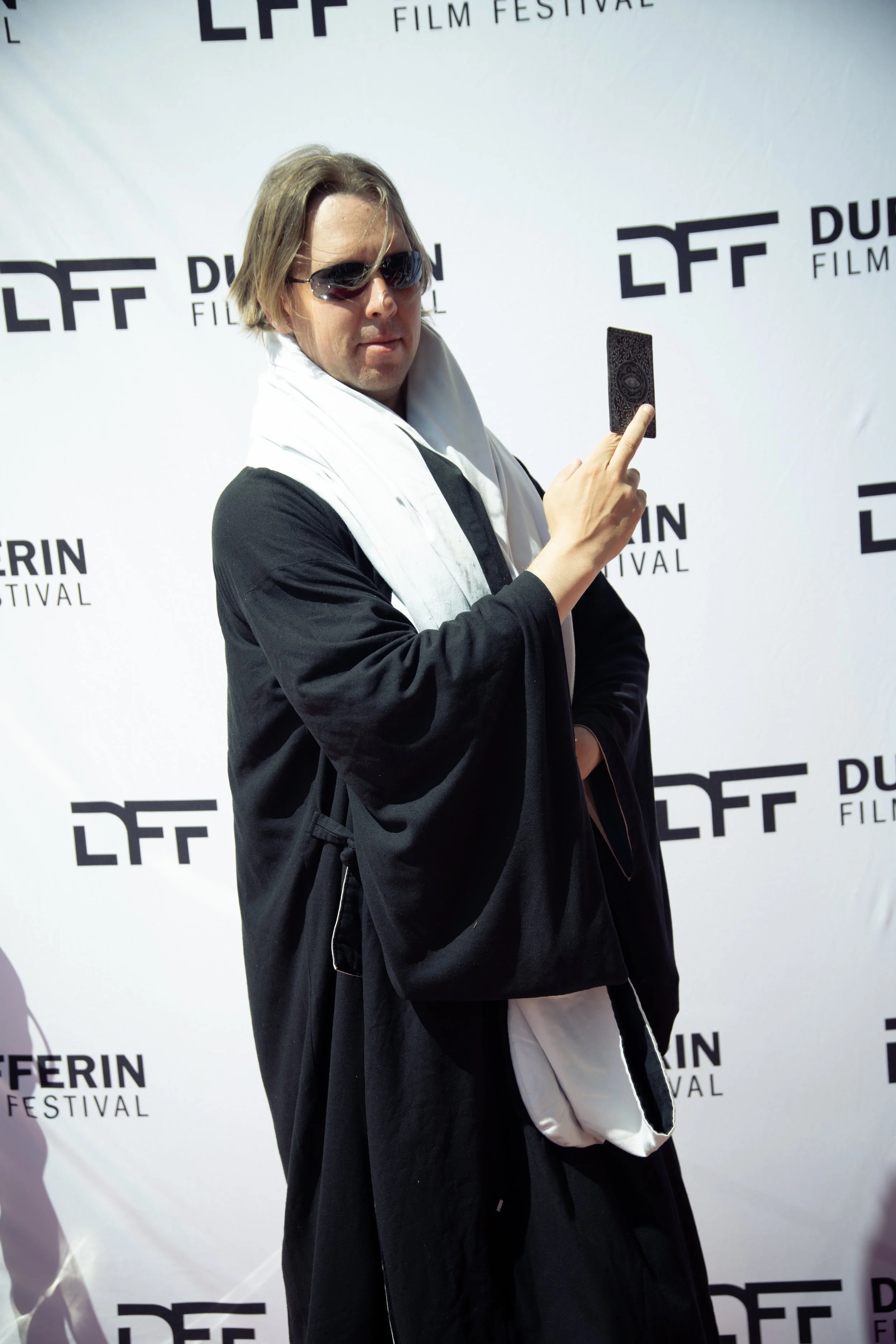 Person wearing sunglasses and black robe with white scarf poses at Dufferin Film Festival event backdrop.
