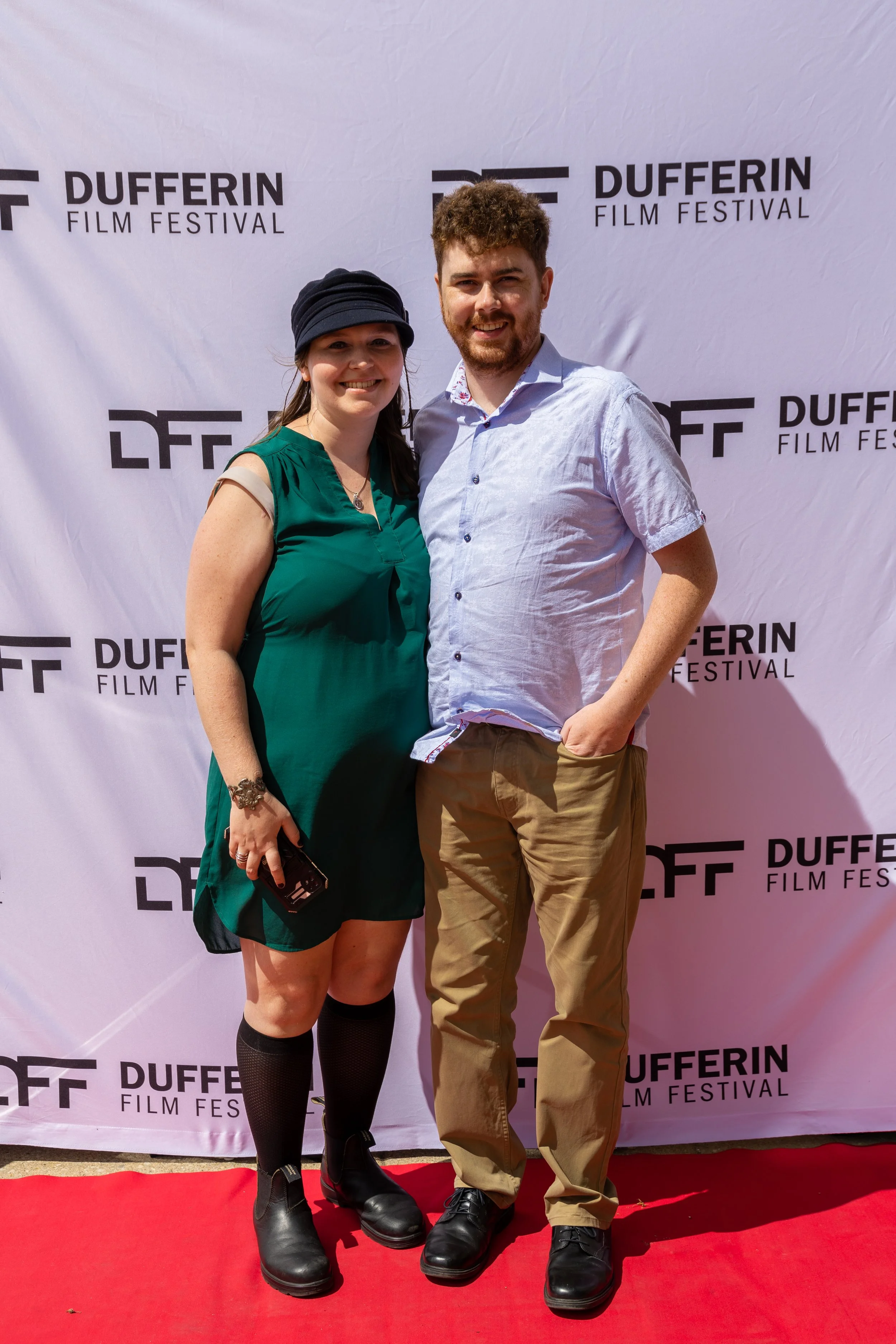 A woman and a man posing on the red carpet at the Dufferin Film Festival in front of a branded backdrop.