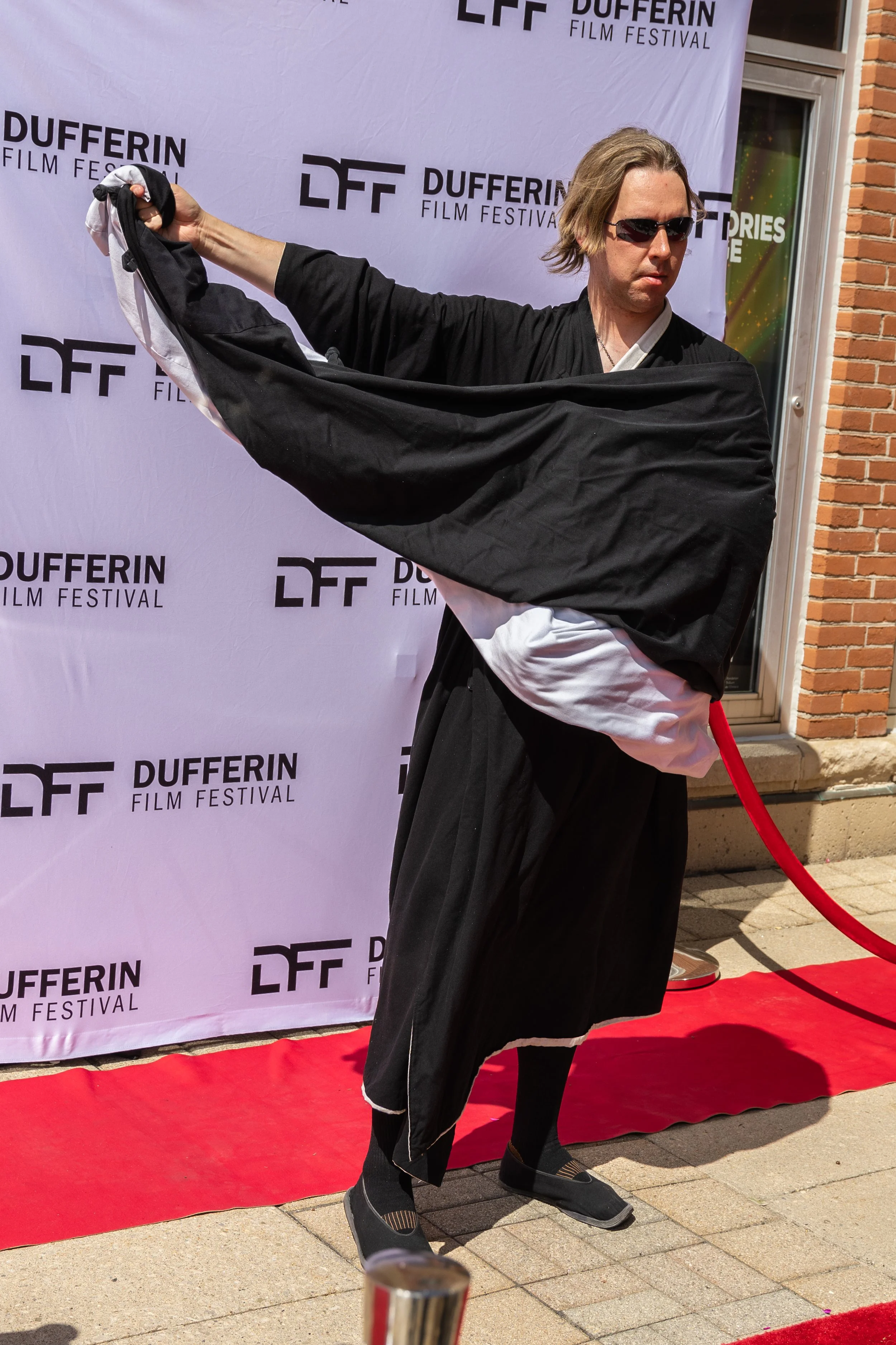 Person in black and white robe posing on a red carpet at Dufferin Film Festival.