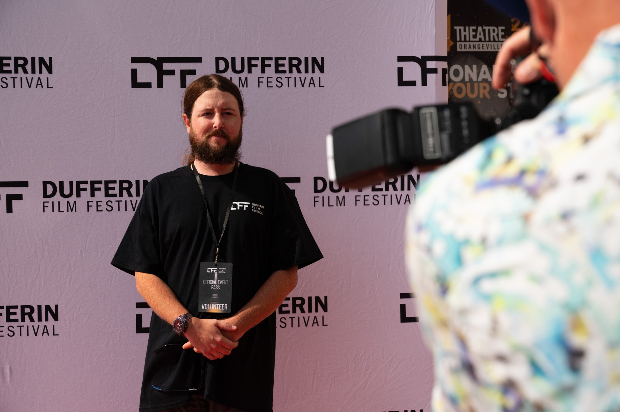 Man posing at Dufferin Film Festival with event badge, camera in foreground.
