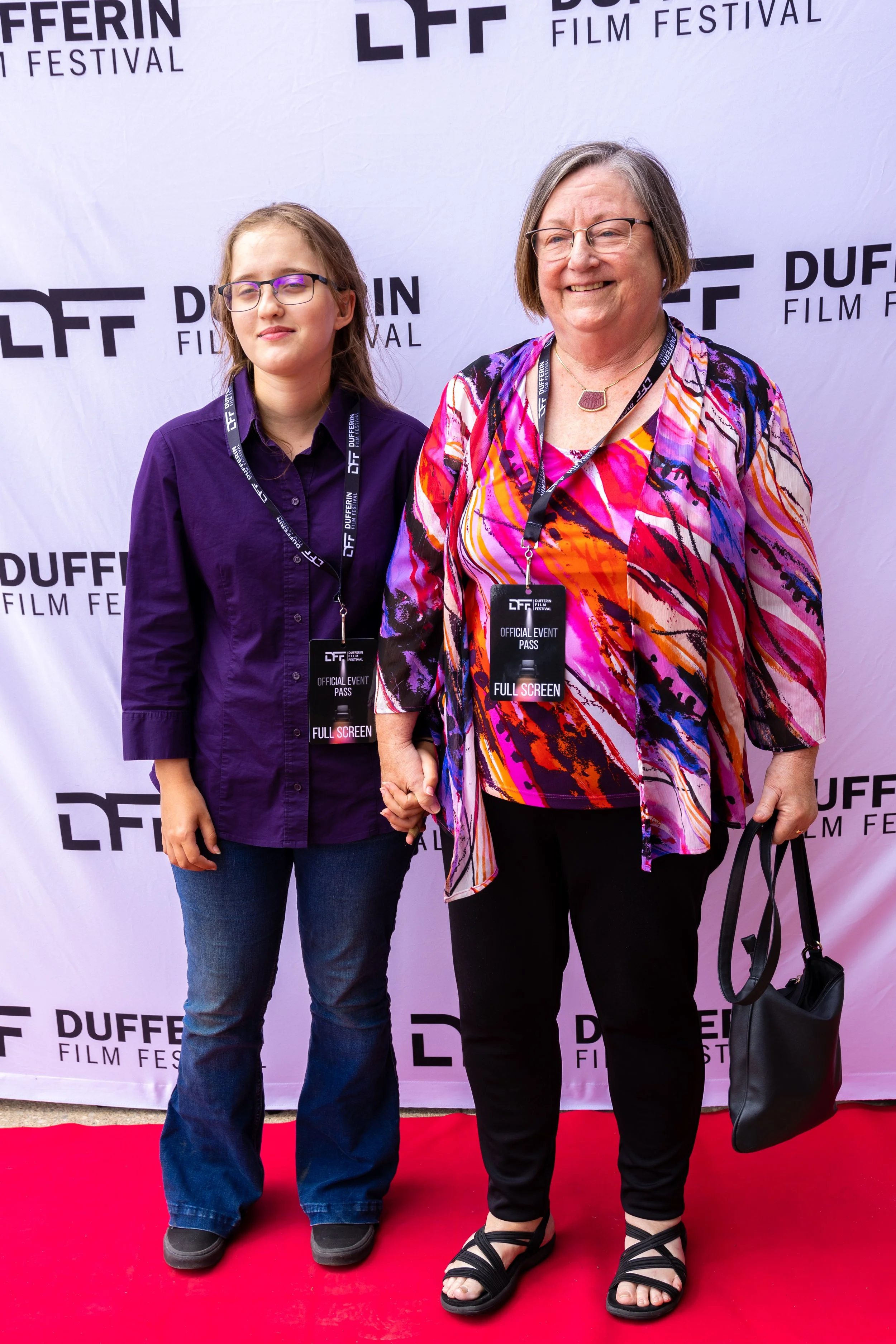Two people standing on a red carpet holding hands at the Dufferin Film Festival, wearing event badges against a branded backdrop.