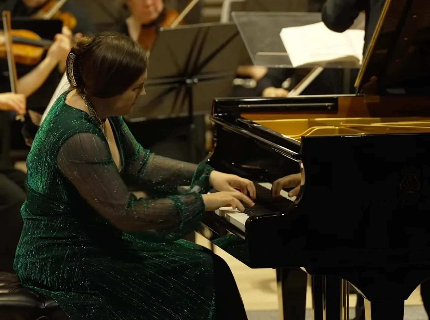 Woman in a dark green dress playing a grand piano during a musical performance.