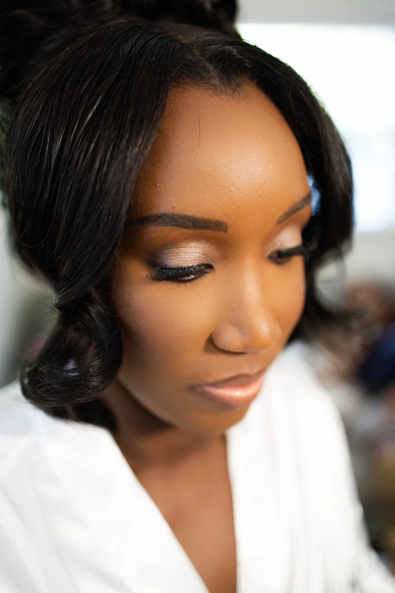 Close-up of a woman's face with styled black curly hair, wearing makeup including eyeshadow, eyeliner, and lipstick, dressed in a white garment.
