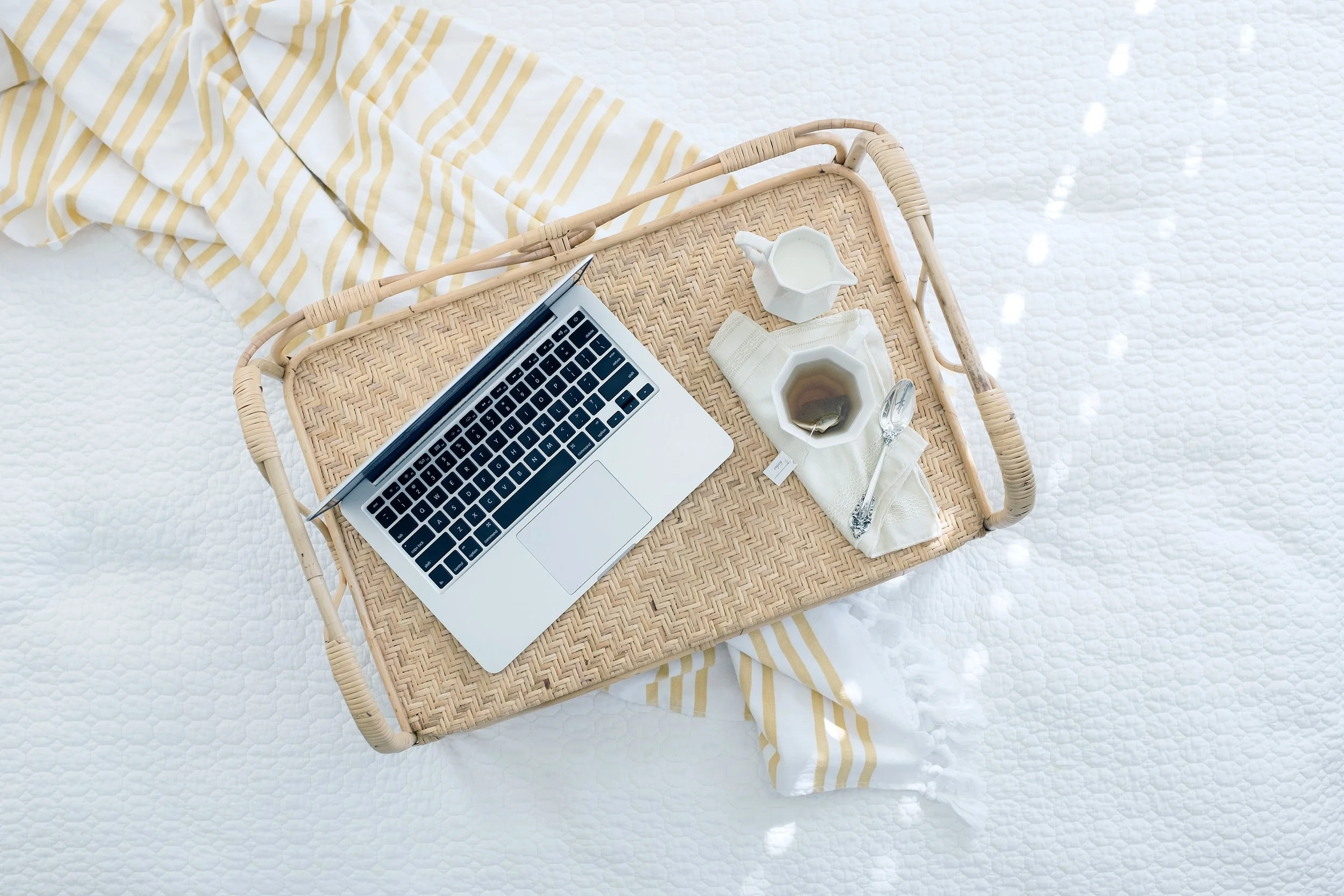 computer sitting on woven tray next to coffee and creamer