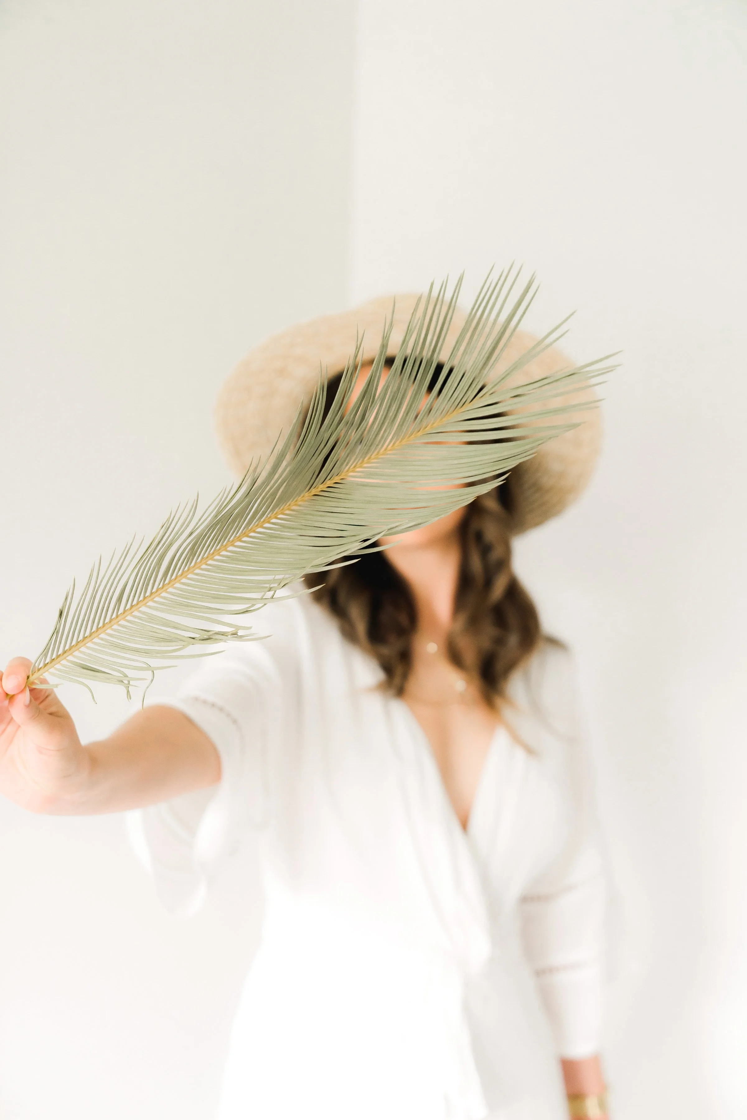 woman in hat holding giant feather across face