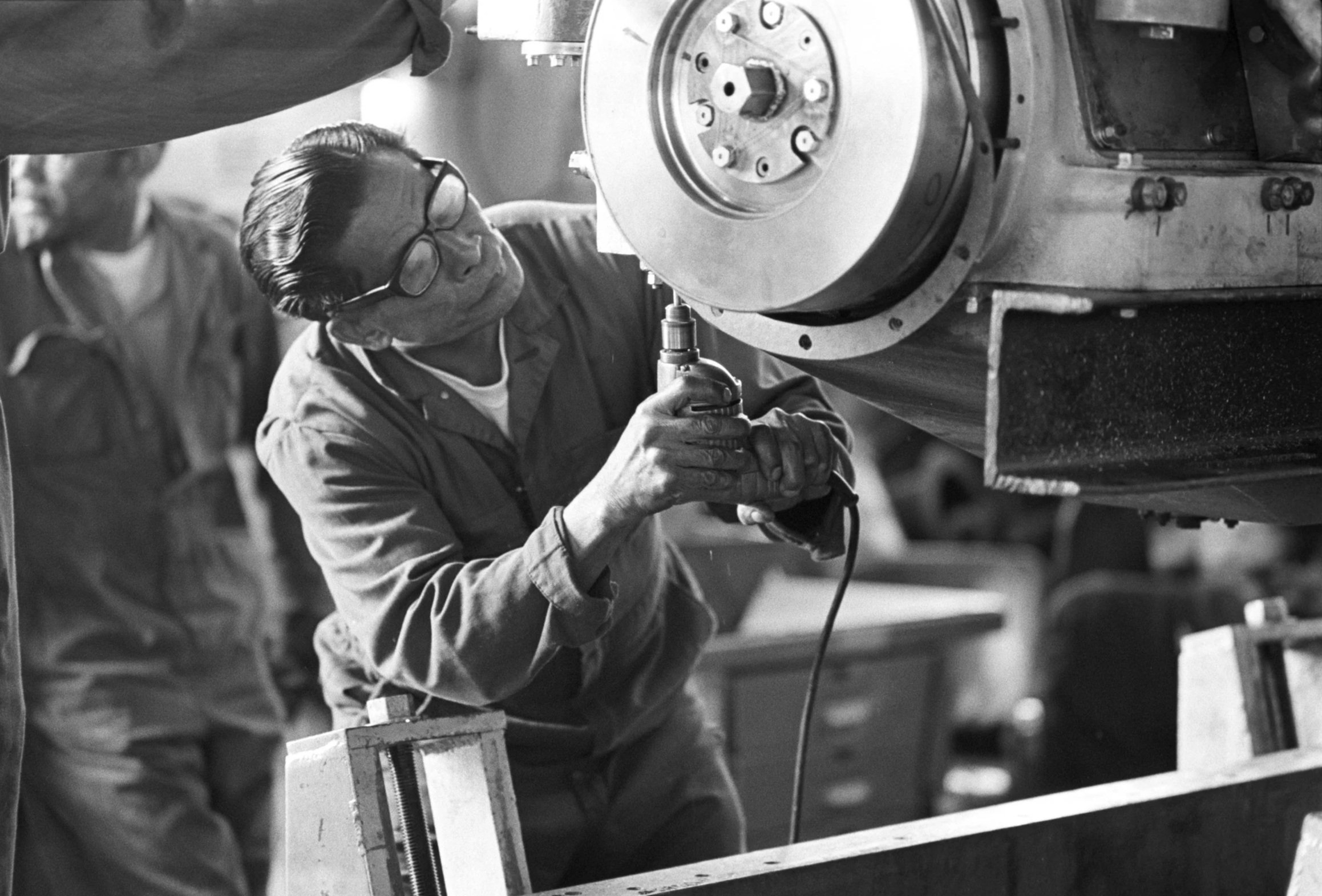 Long Beach Naval Shipyard (1972),
Two factory workers working together on a piece of factory equipment at the Long Beach Naval Shipyard factory.
Photographed by Alan Ohashi