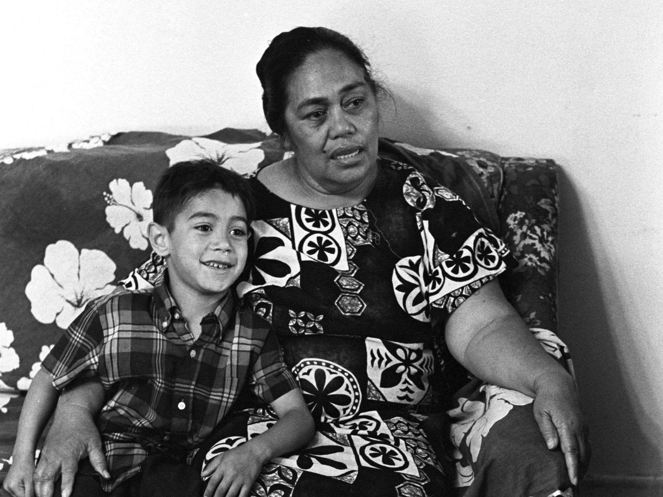 Mrs. Sialoi and Boy Sitting on Couch (1972), Mrs. Sialoi and a boy sitting on the couch in her and Reverend Sialoi's residence.
Photographed by Alan Ohashi