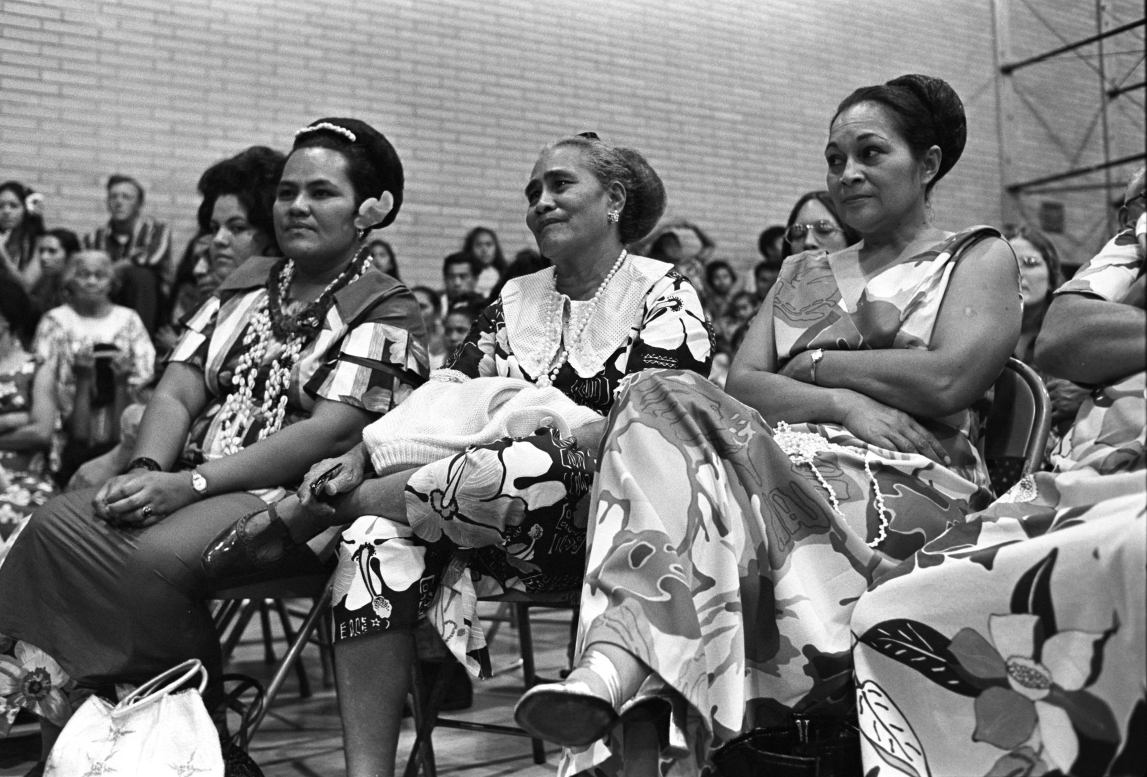 Luau Audience Watching Dancers (1972),
Audience members seated on chairs and on the floor of a basketball court, watching a traditional dance performance at a luau.
Photographed by Alan Ohashi