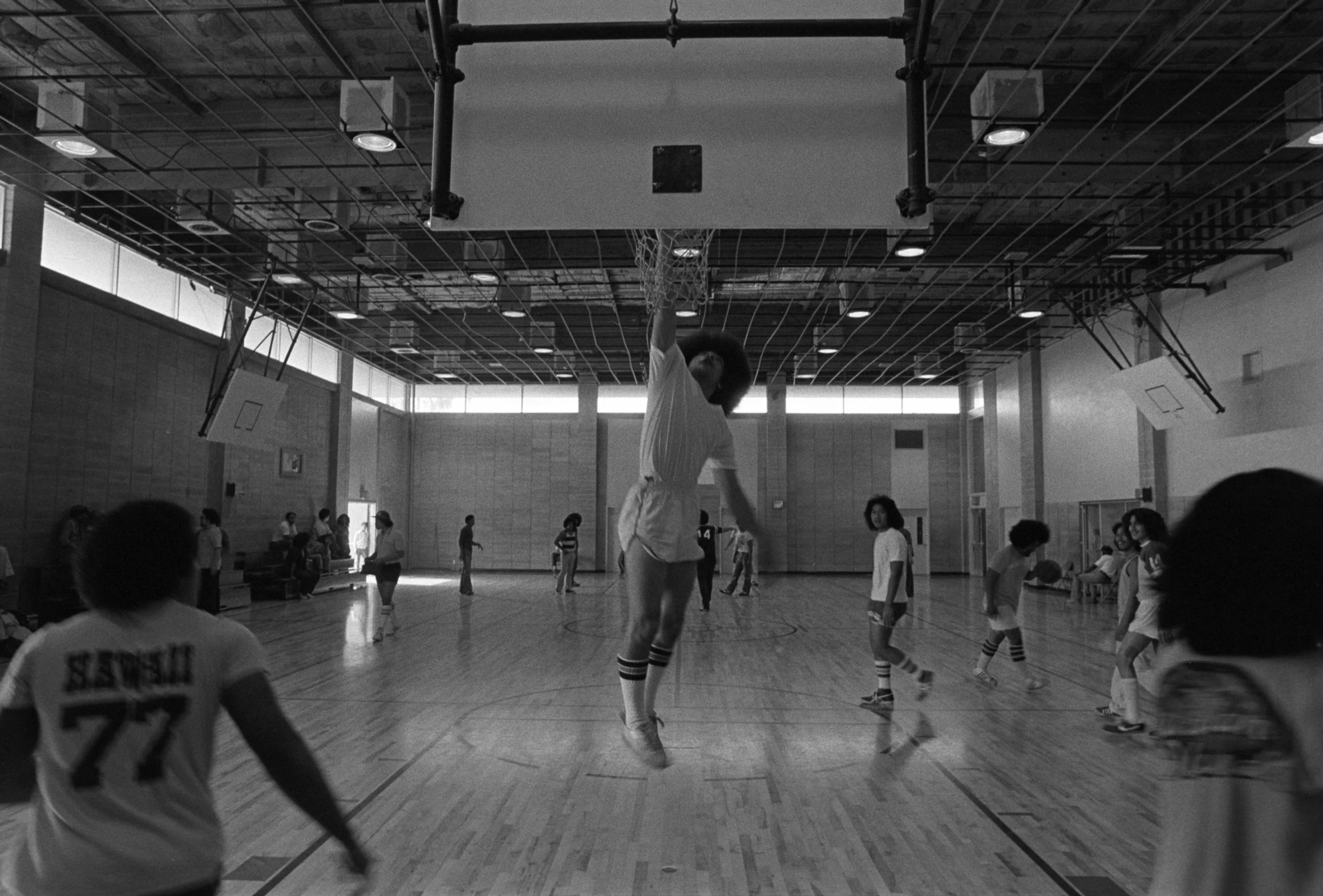 Omai Fa'atasi - Basketball in Carson (1977-1978),
A view behind the backboard of a basketball player jumping and shooting the ball.
Photographed by Visual Communications