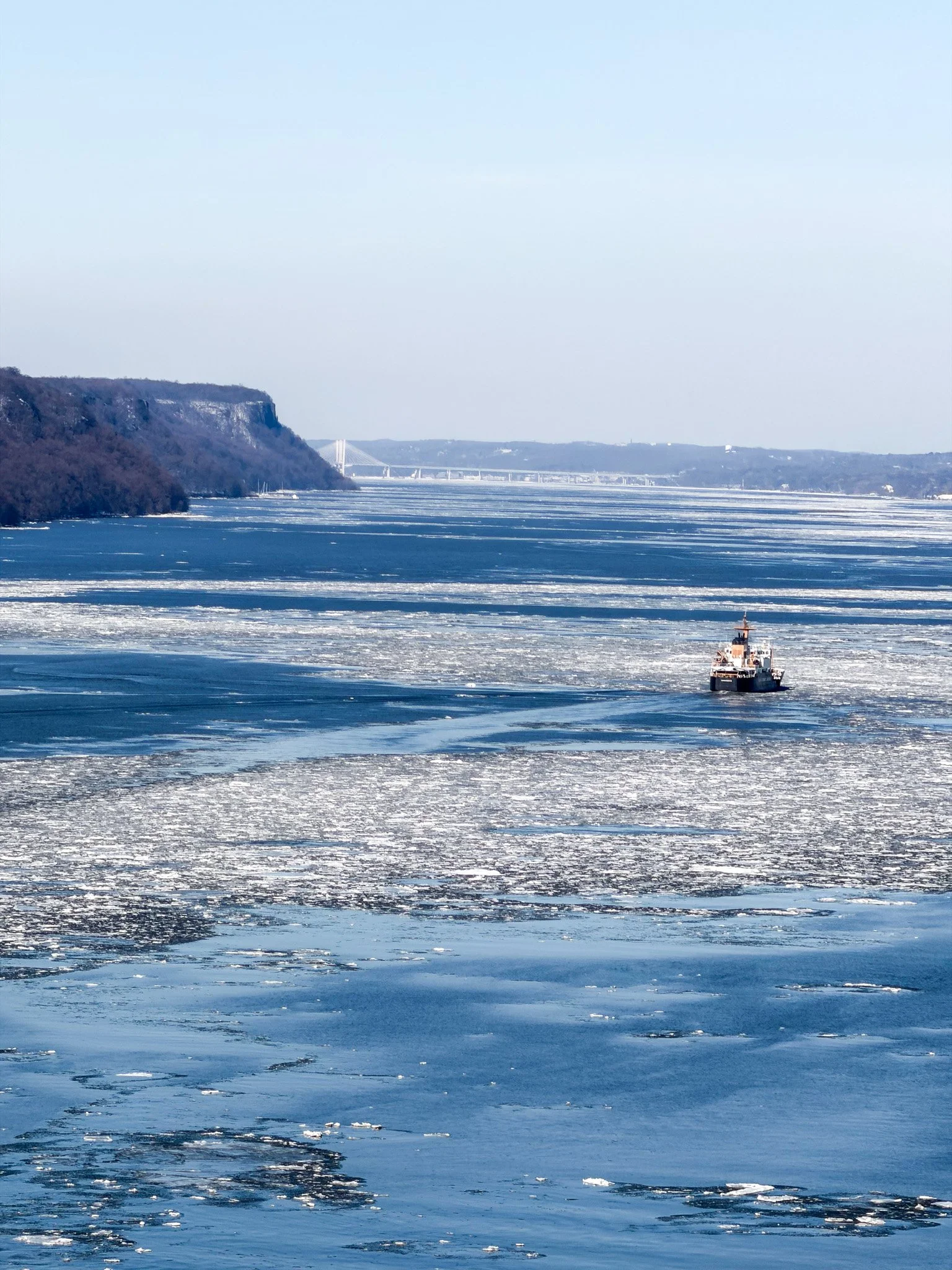 A boat navigating through icy water with land and cliffs in the background.