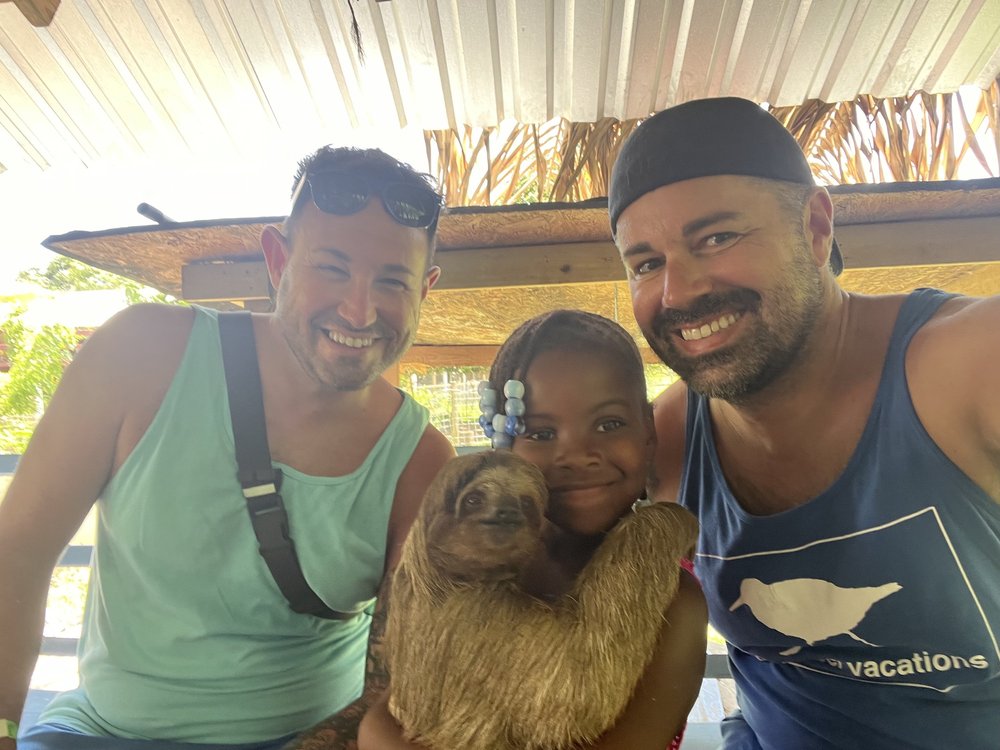 Sandpiper Vacations founders Sean and Nick Bryan with their daughter Piper holding a sloth