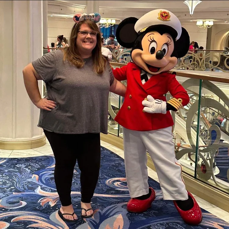 A woman standing next to a person in a Mickey Mouse costume dressed as a ship captain, in a decorated indoor setting, both smiling at the camera.