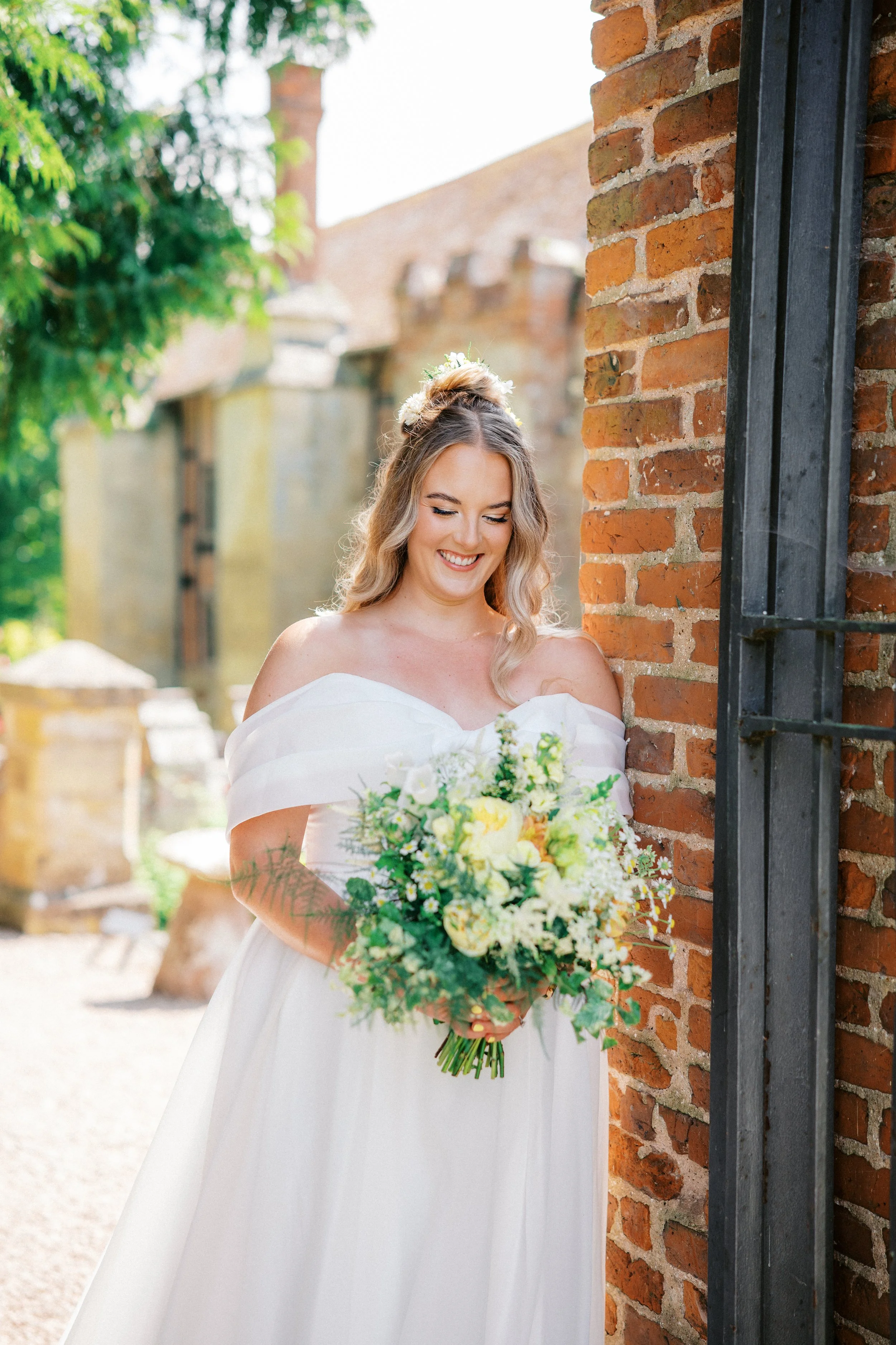 Bride leaning against brick wall holding a bouquet of yellow and green flowers