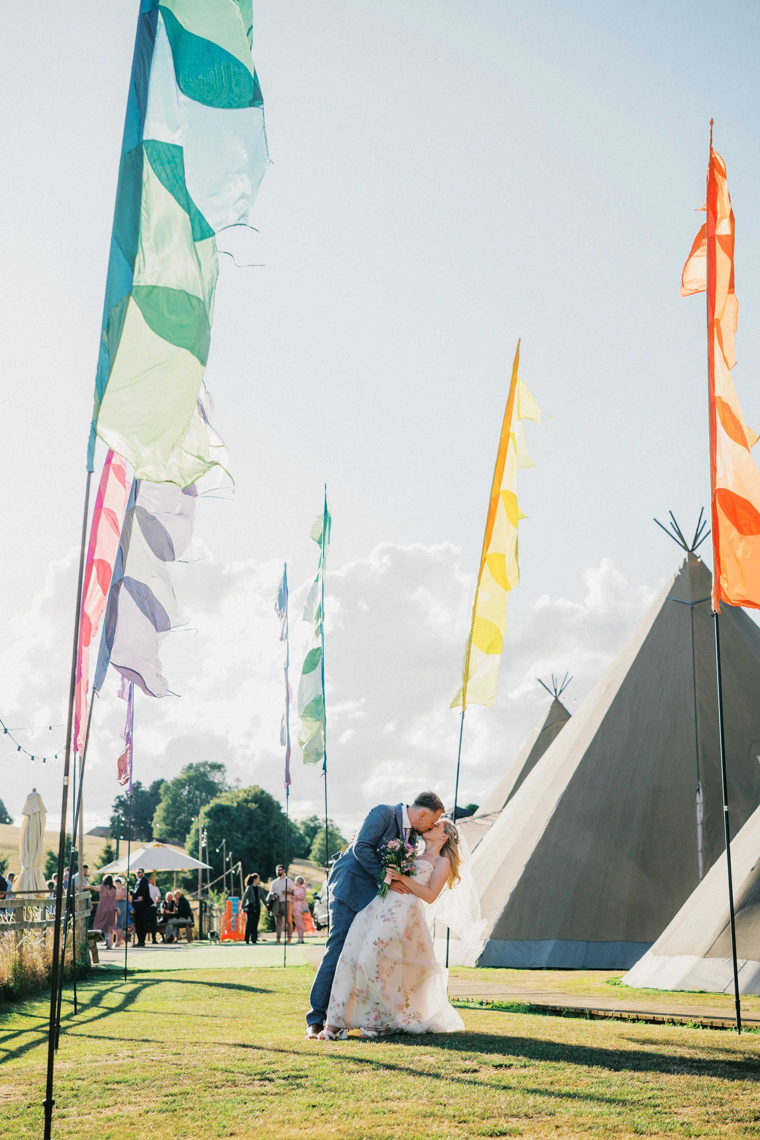 Wedding Couple sharing a kiss surrounded by festival flags and with a tipi tent behind. wedding venue is Hadsham Farm
