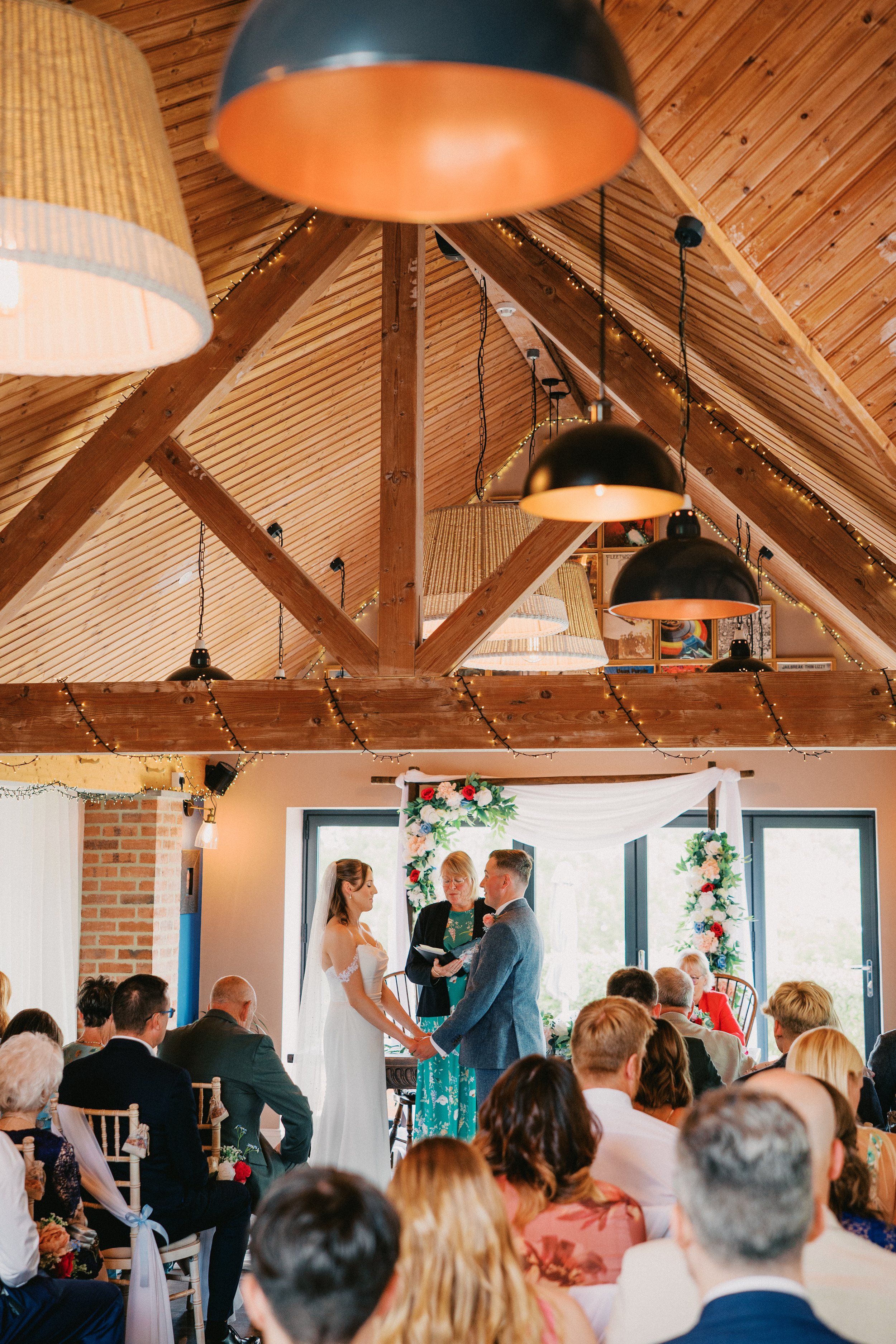 wedding ceremony in large room with wooden beams. The bride and groom holding hands and sharing vows.