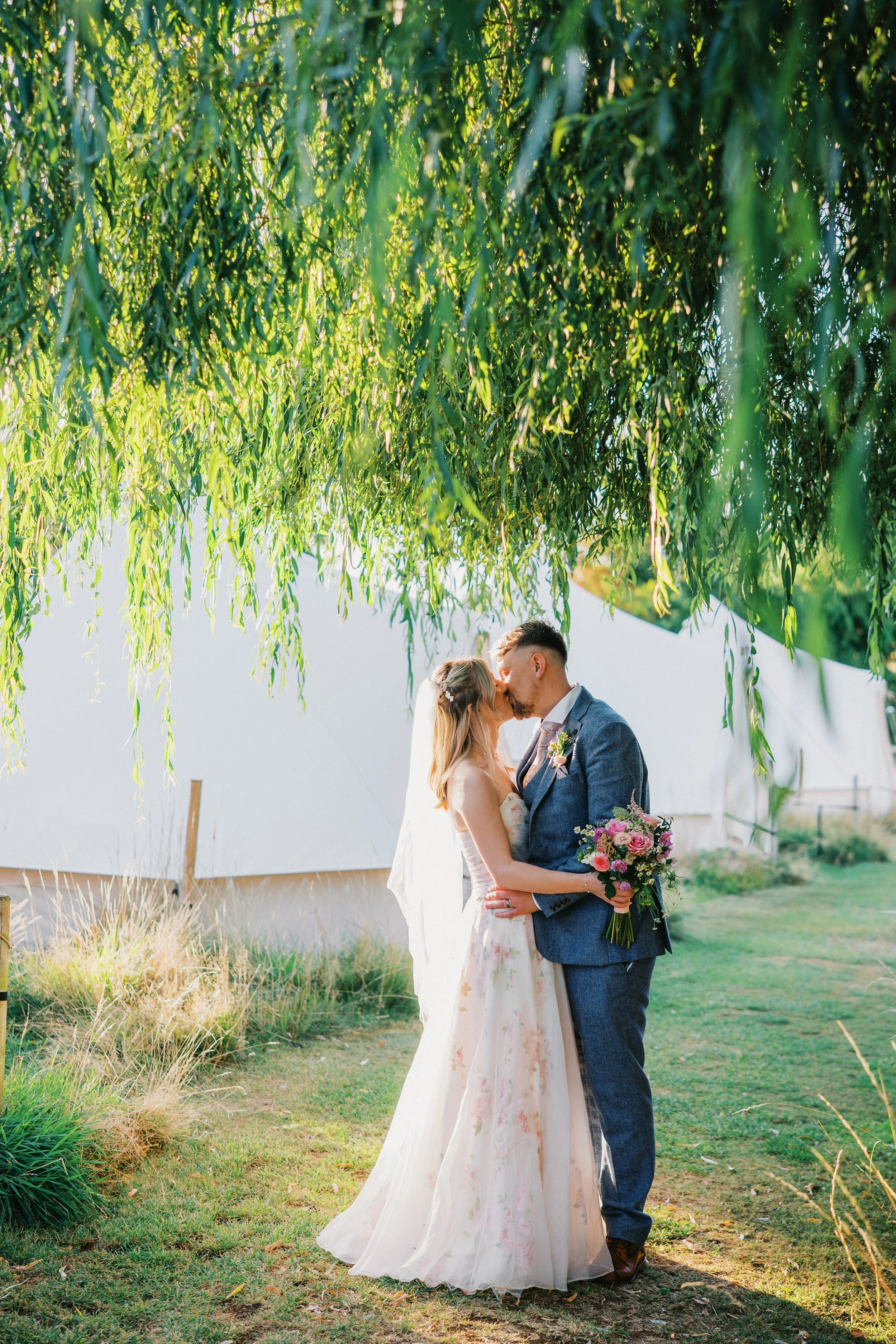 wedding couple stood under a willow tree sharing a kiss at hadsham farm