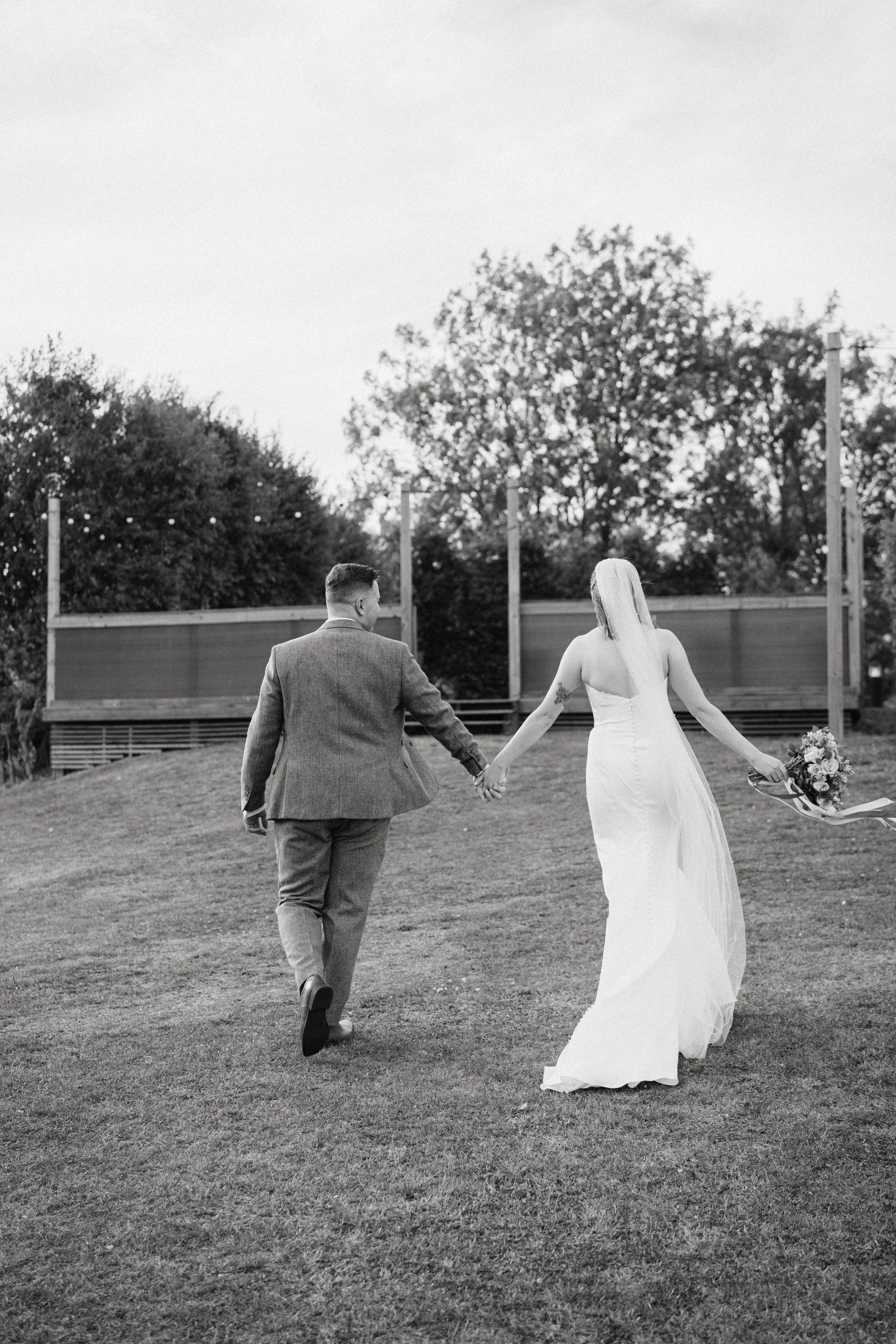 black and white photo of bride and groom holding hands and walking together