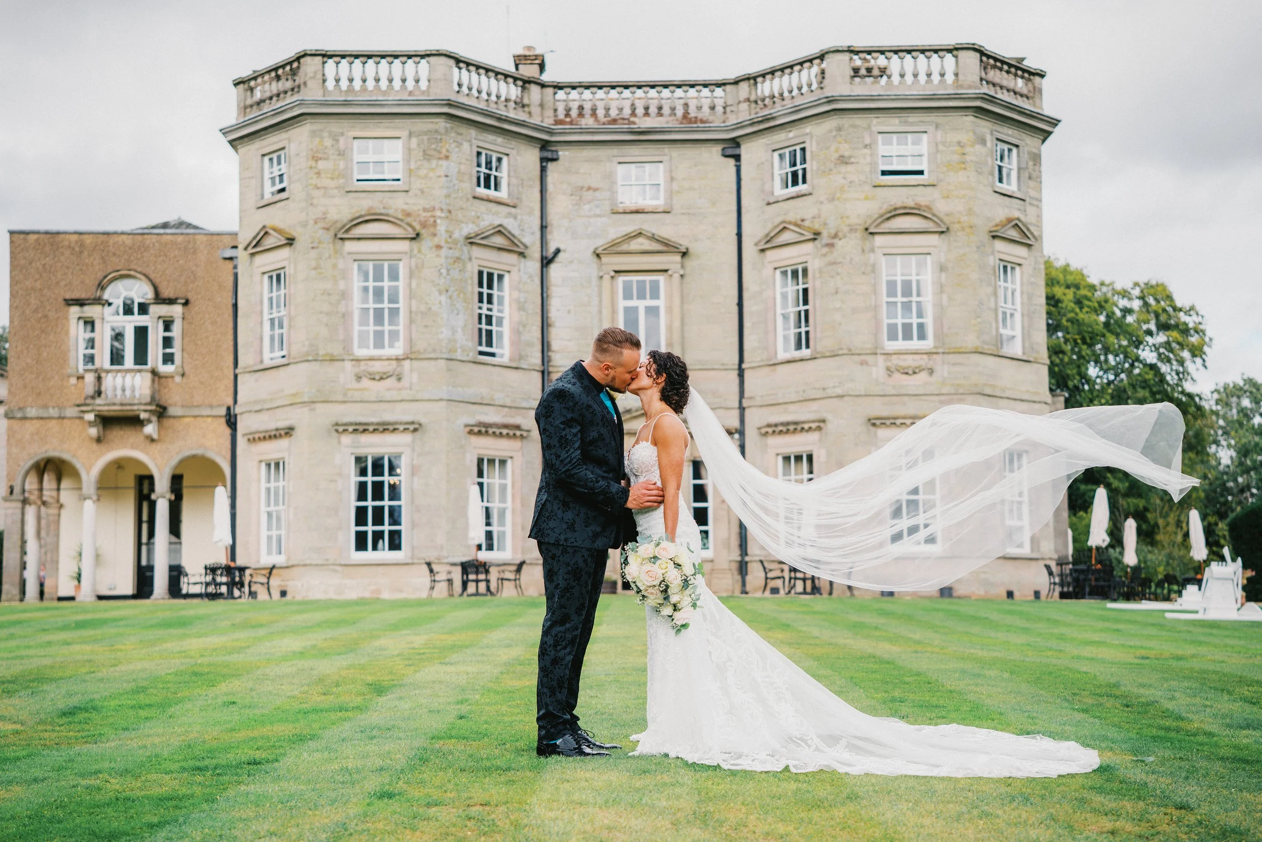 Bride and Groom kissing in front of mansion - Bourton Hall wedding venue