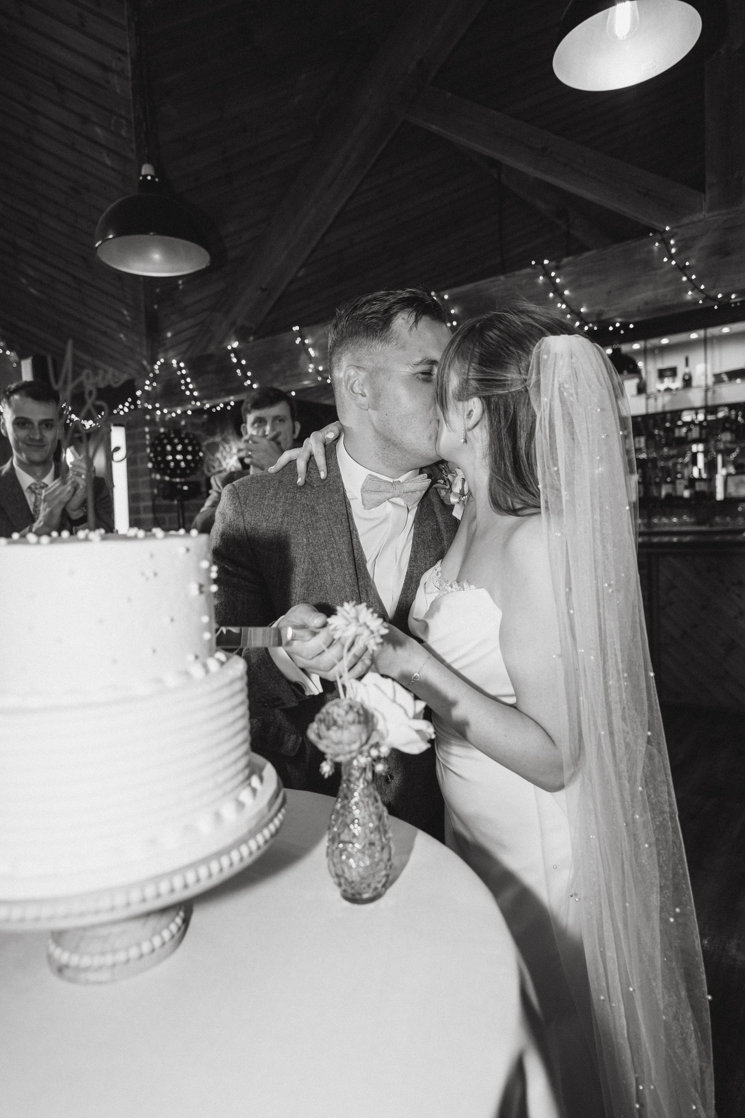 black and white photo of couple kissing and cutting a cake