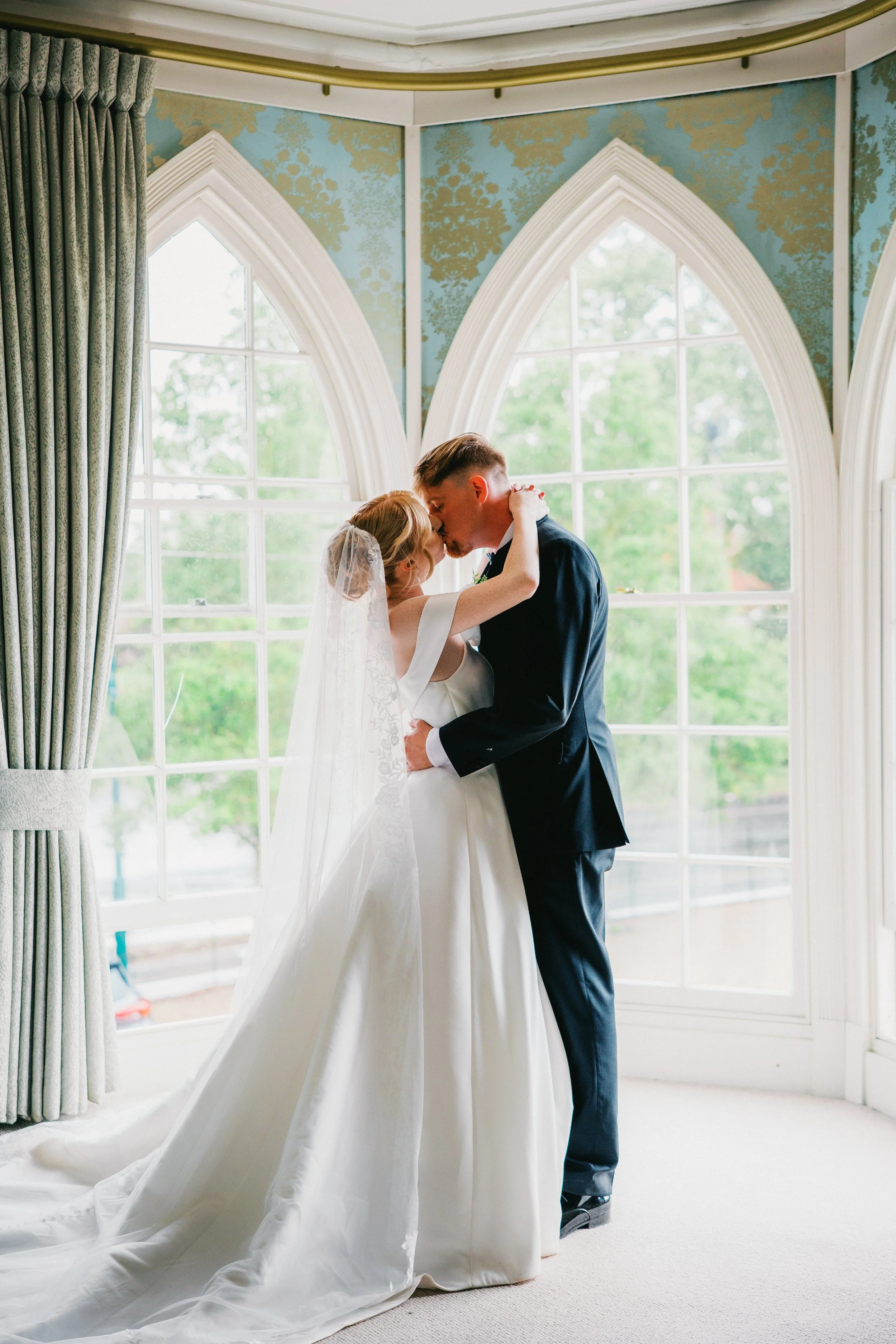 Wedding Bride and Groom in bright room with arched white windows embracing eachother and kissing. Venue is Warwick House.