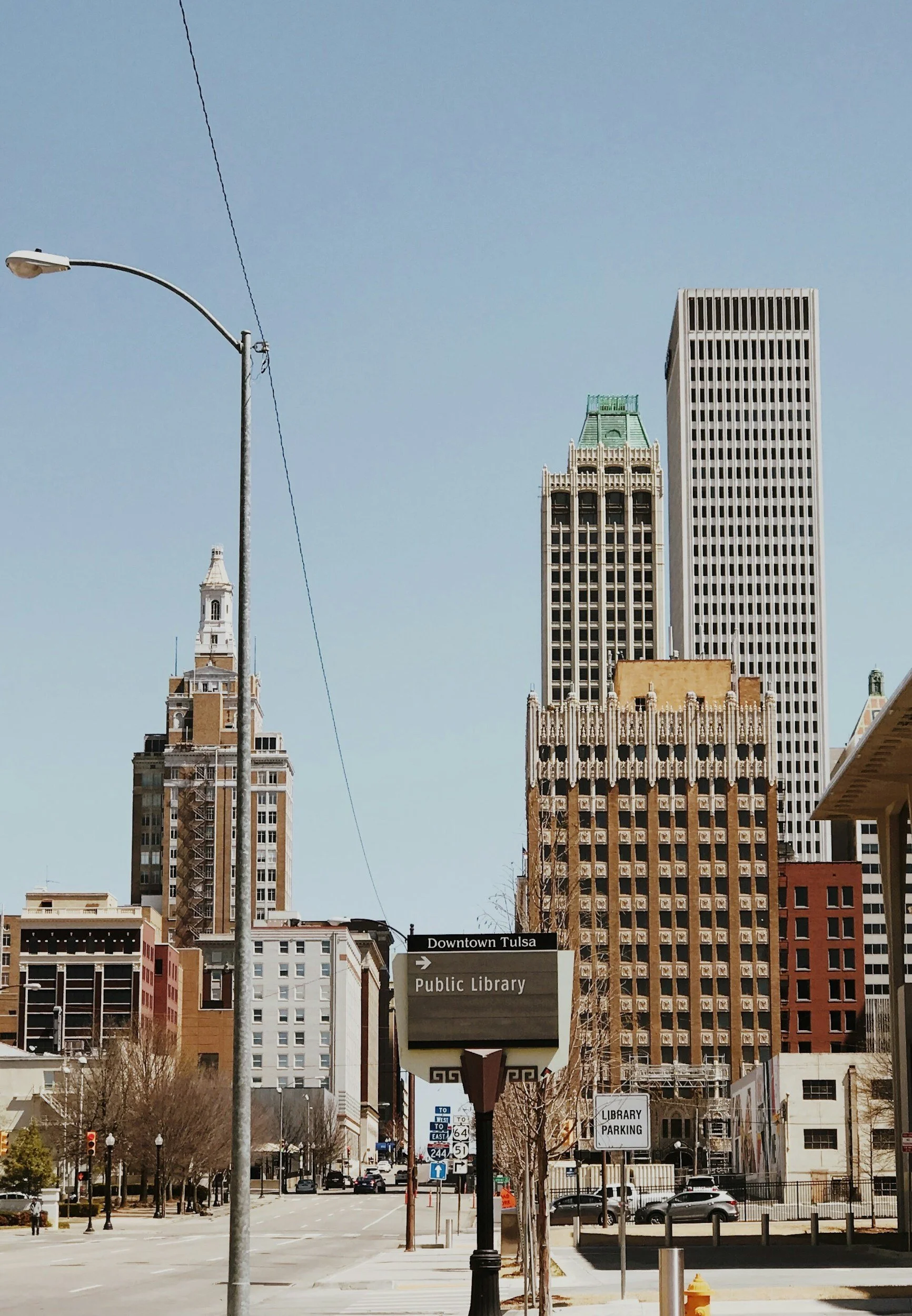 Cityscape of downtown Tulsa with tall buildings, street signs, and a clear blue sky.