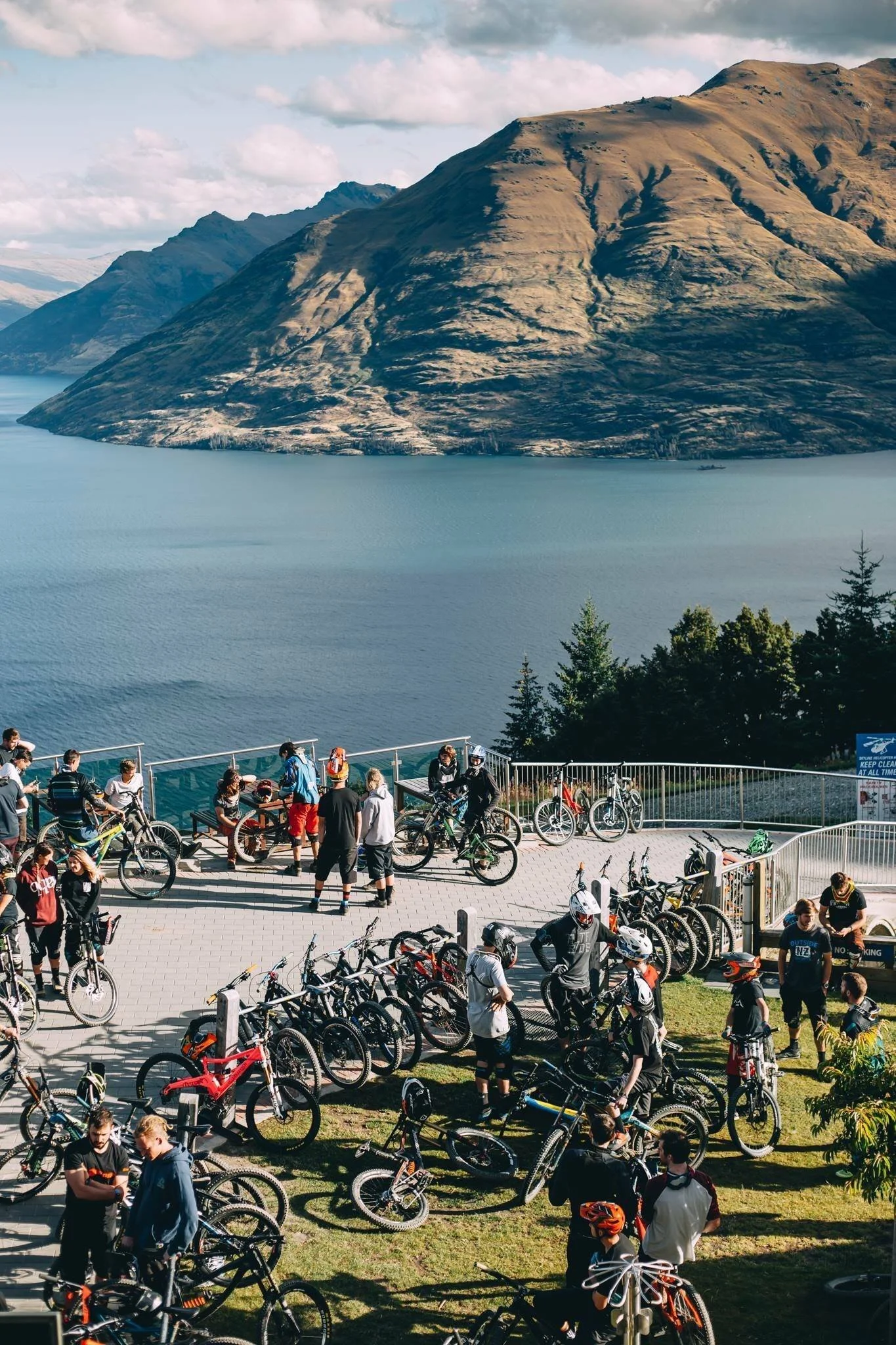 Group of cyclists with mountain bikes on a scenic overlook with a view of a large lake and mountains.