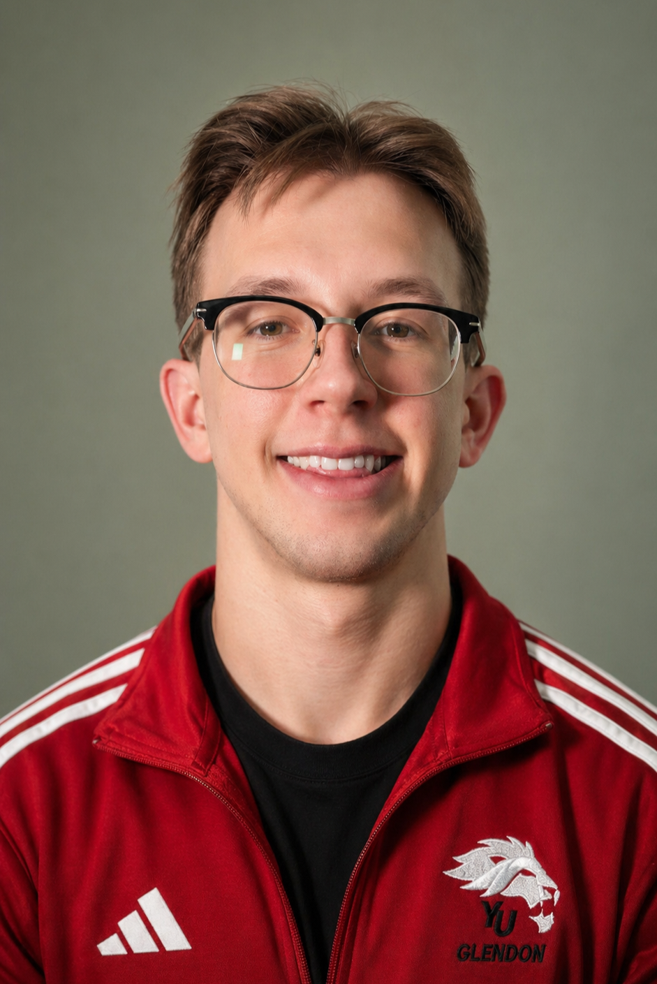 Young man with glasses wearing a red sports jacket with a logo of a lion and the words 'YU GLENDON' on it, smiling at the camera.