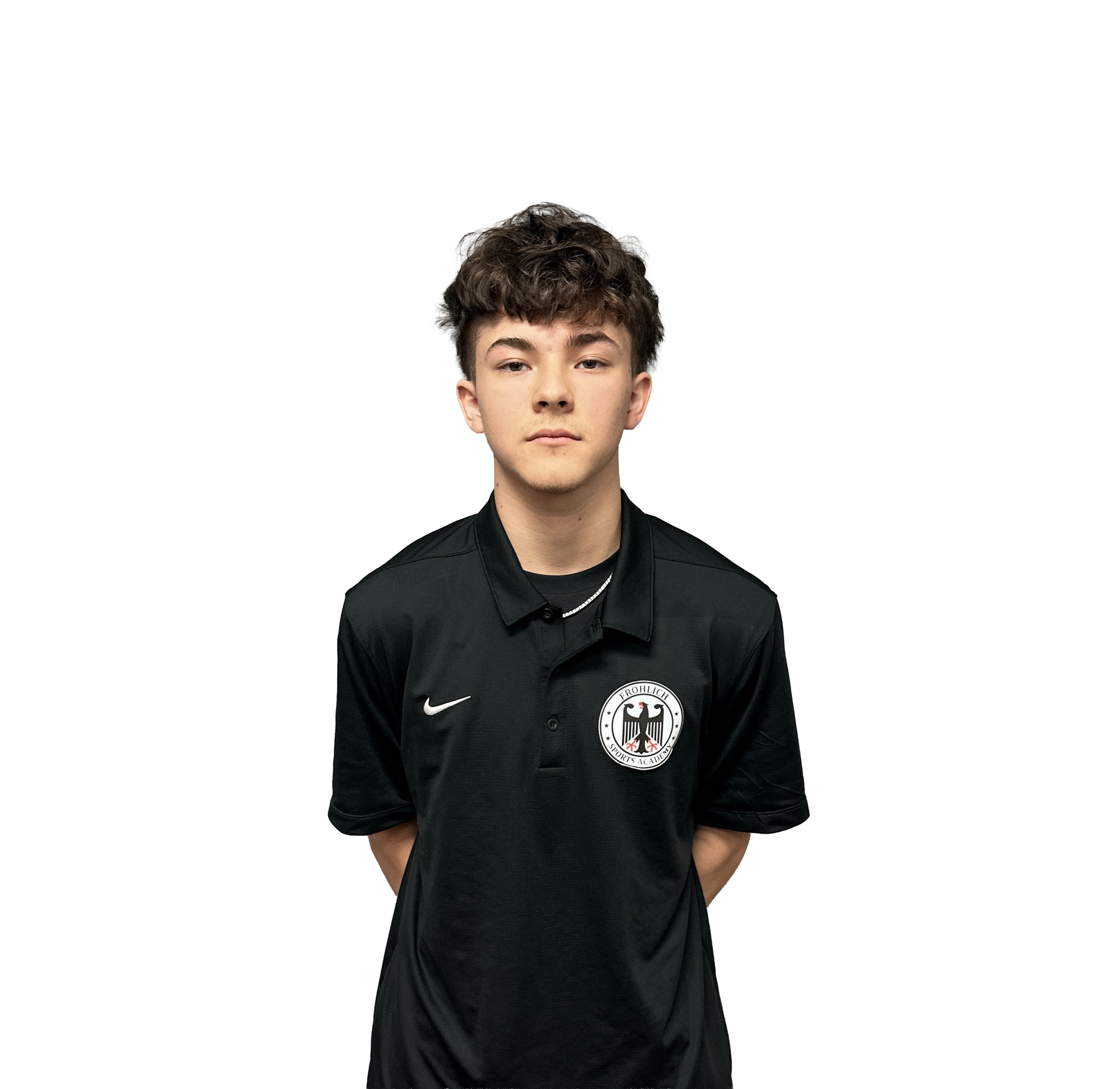 Young man with curly brown hair and light skin wearing a black sports jacket with a German football team logo on the chest, standing against a black background.