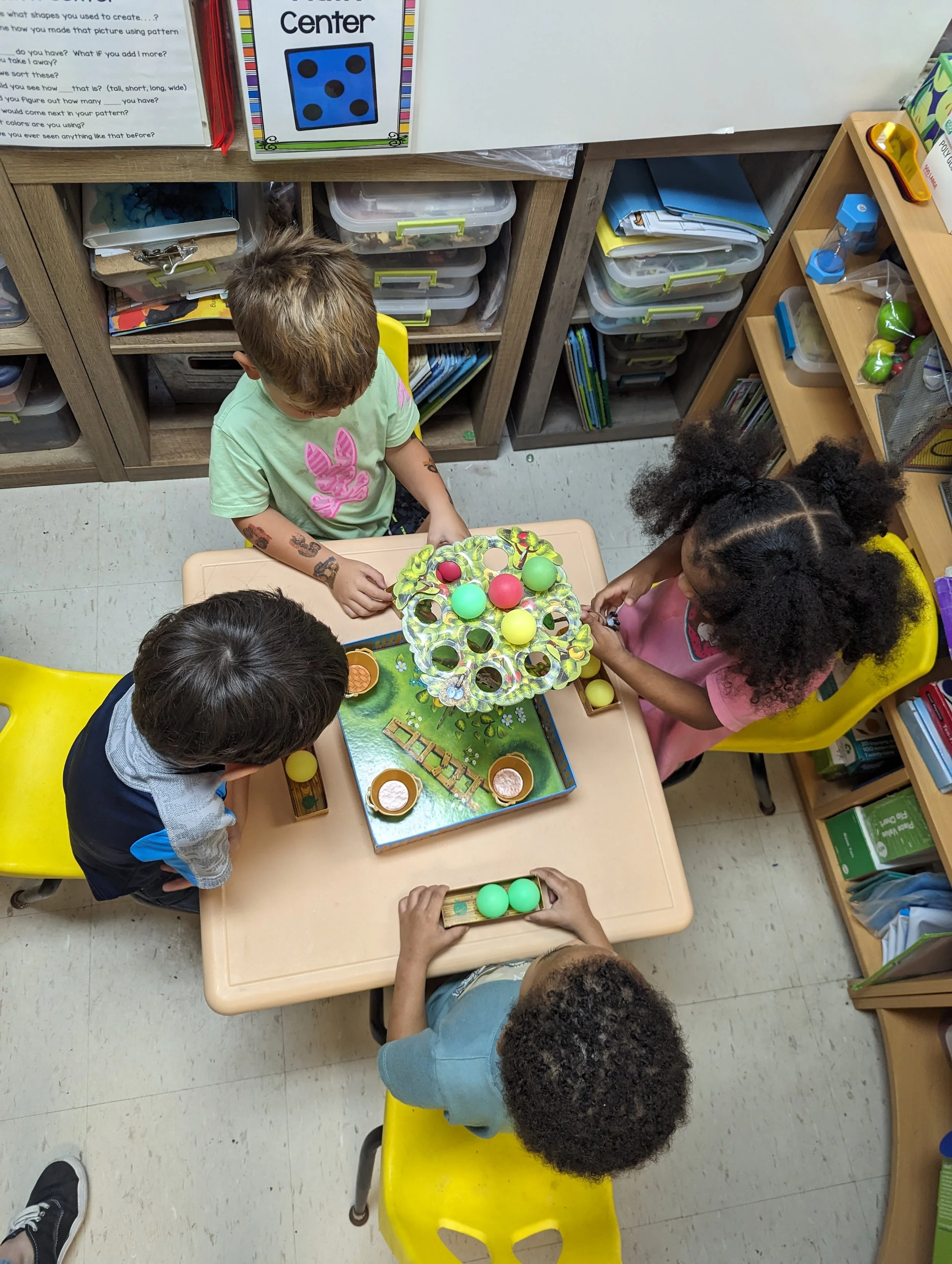 Children playing a game with colored balls and a tiered stand in a classroom.