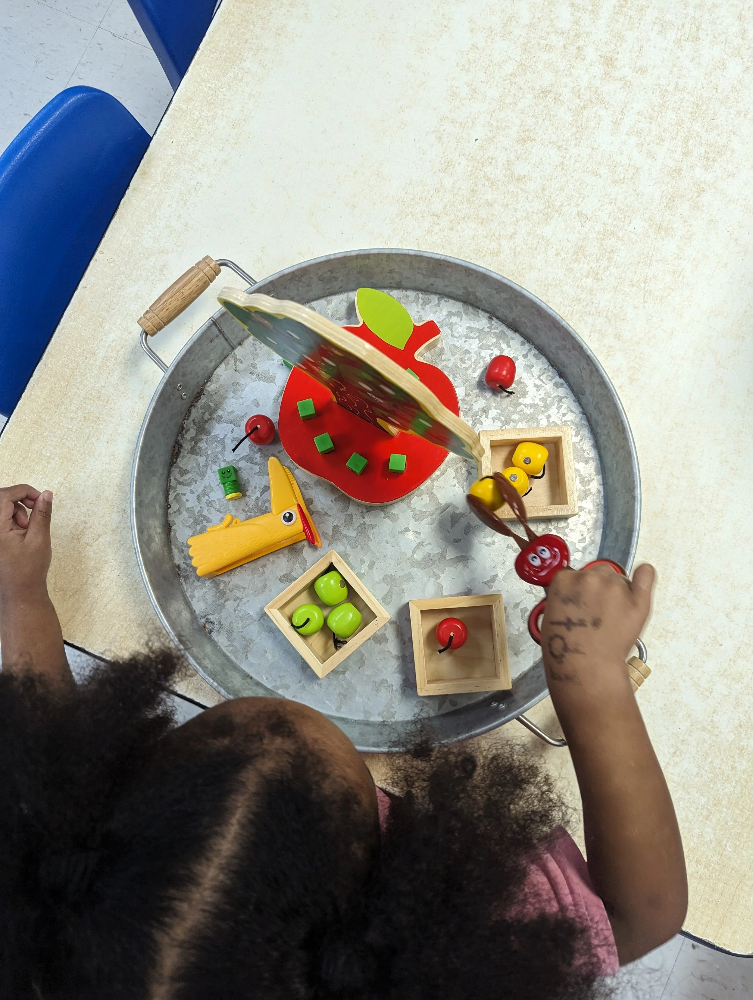 Child playing with wooden toy set, including red and green apples.