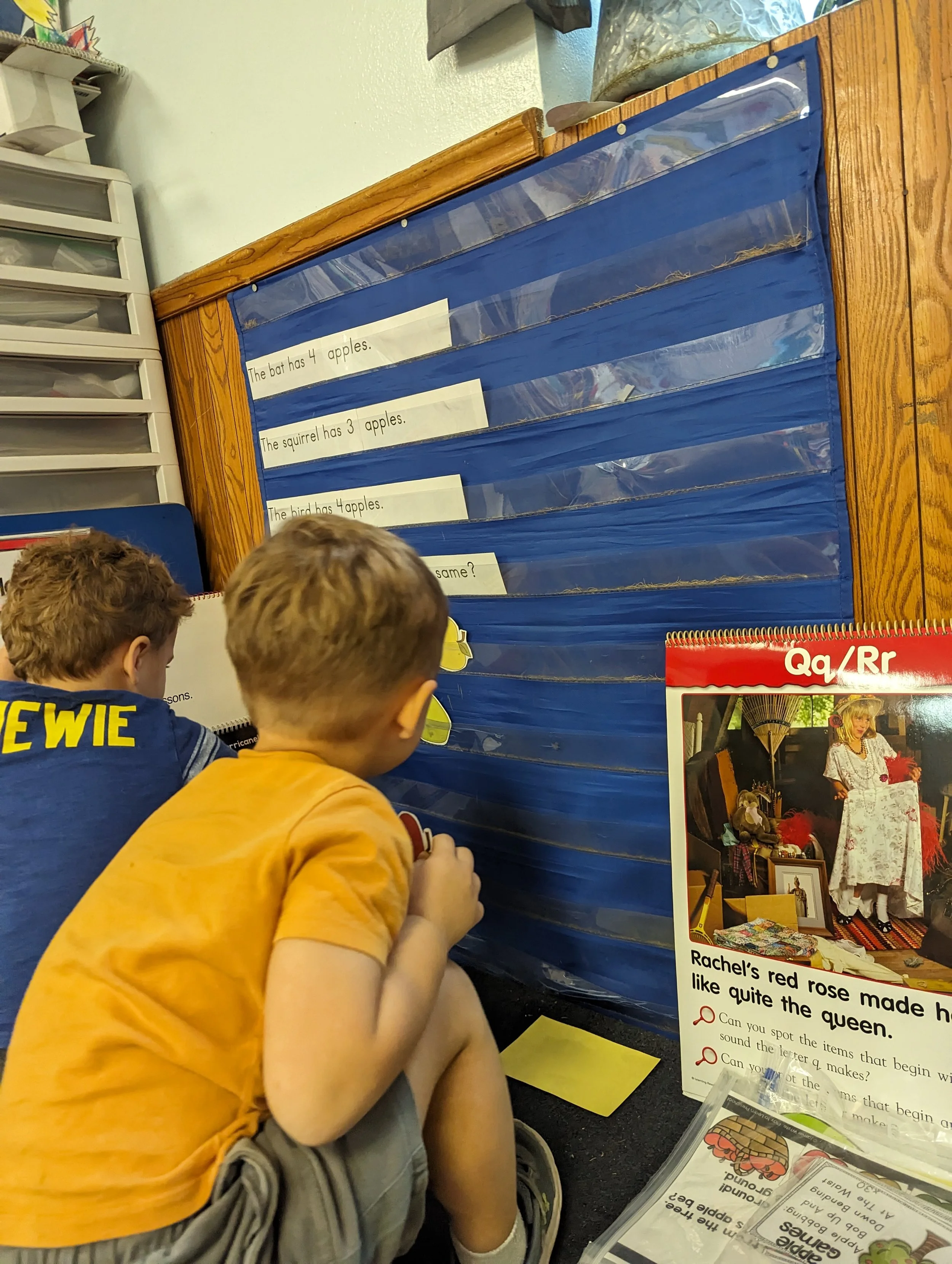 Two young boys looking at a blue class pocket chart.