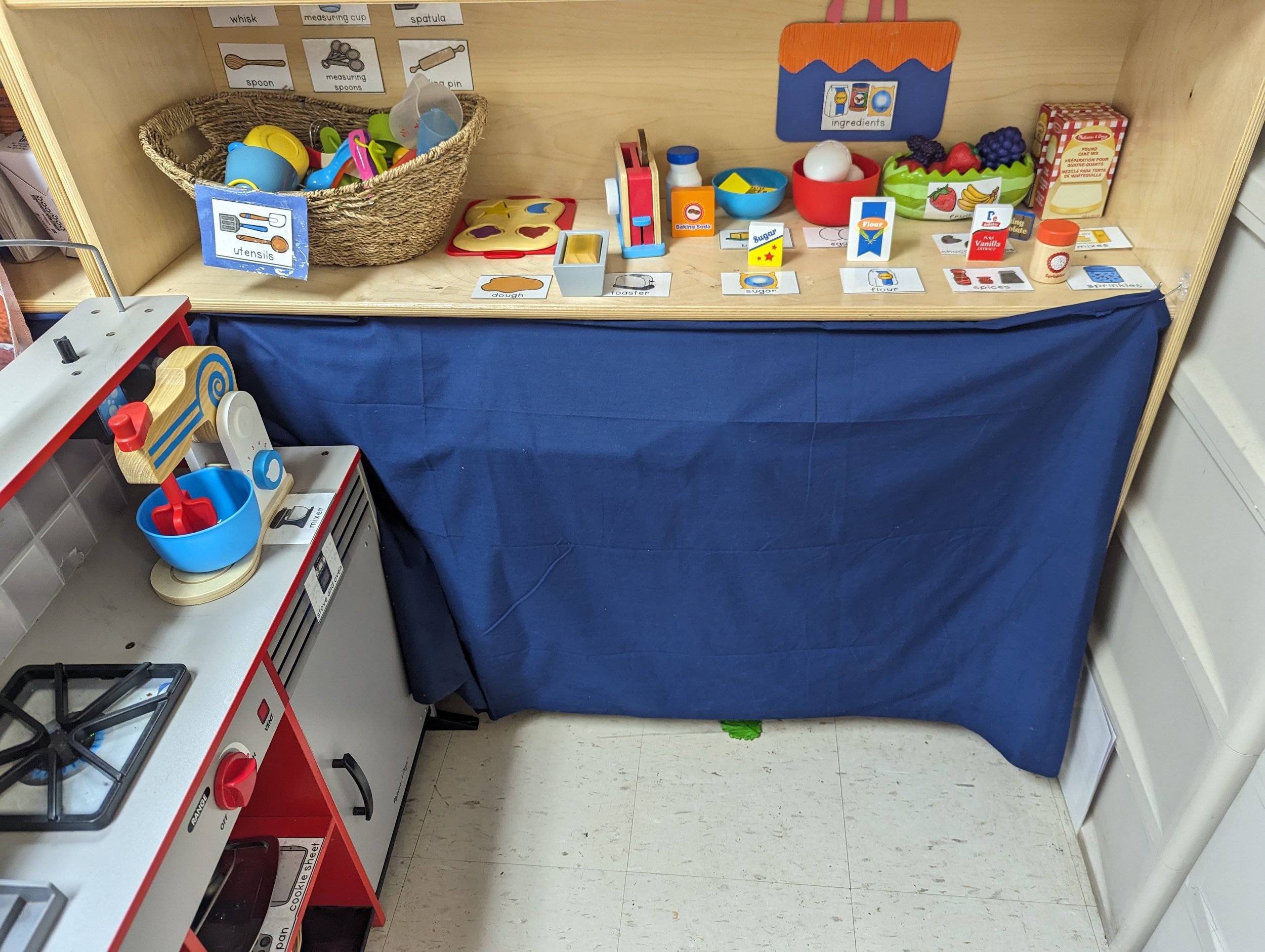 A children's play kitchen and food pretend play set with toy utensils, pans, and various miniature food items on a wooden table.