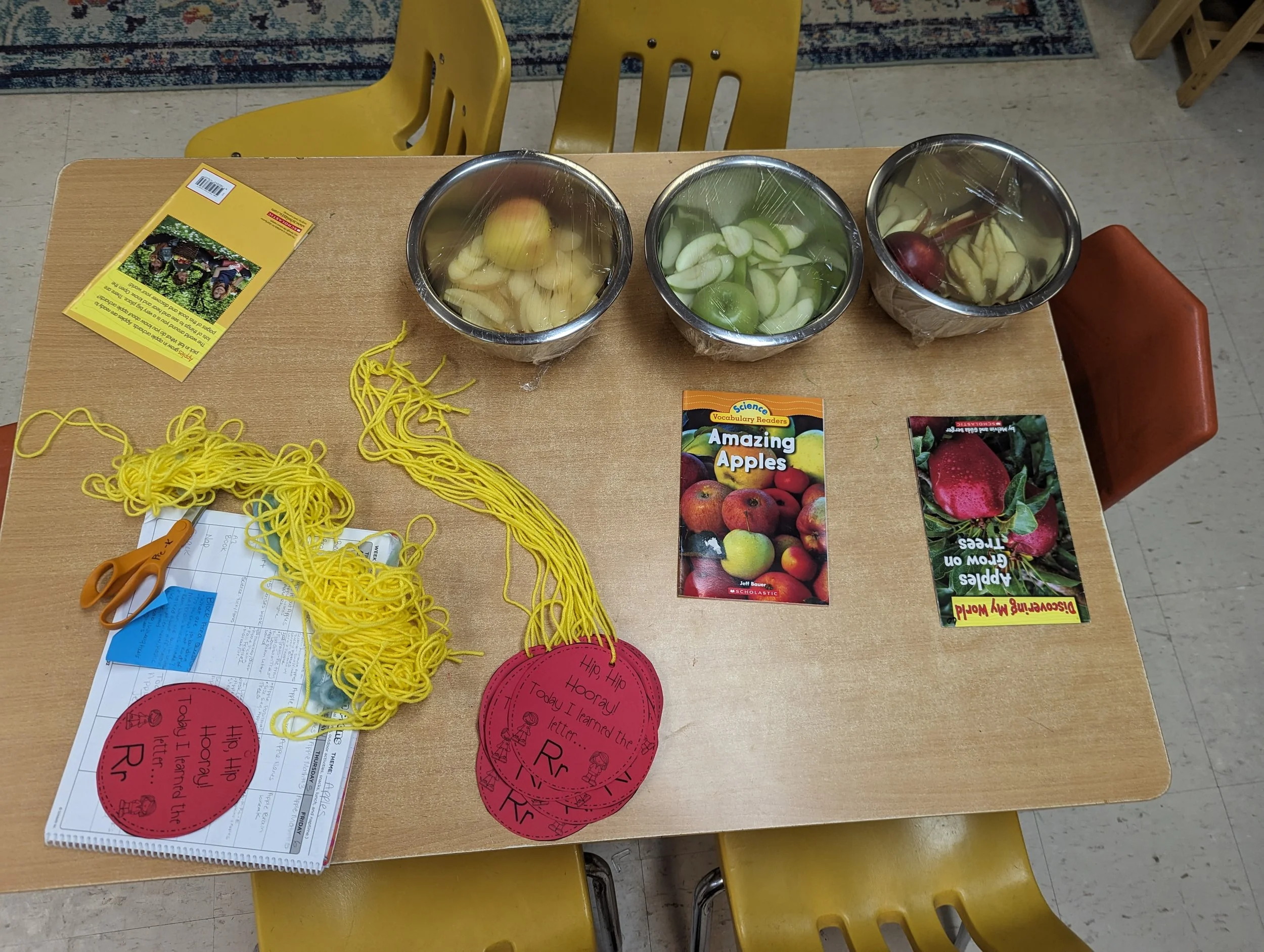 A classroom table displaying sliced apples and children's books.