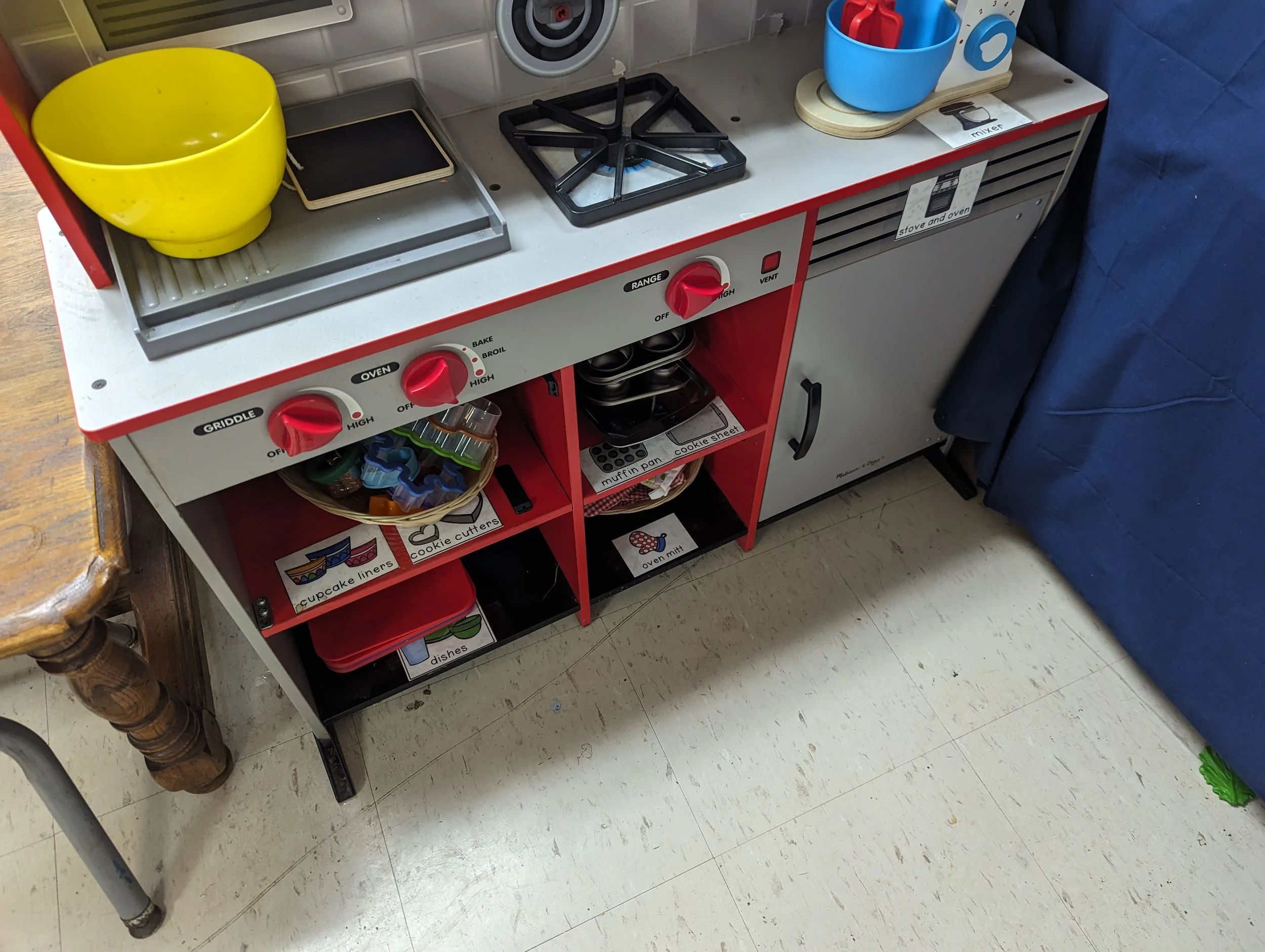 A children's play kitchen set with toy stove, oven, and storage compartments.