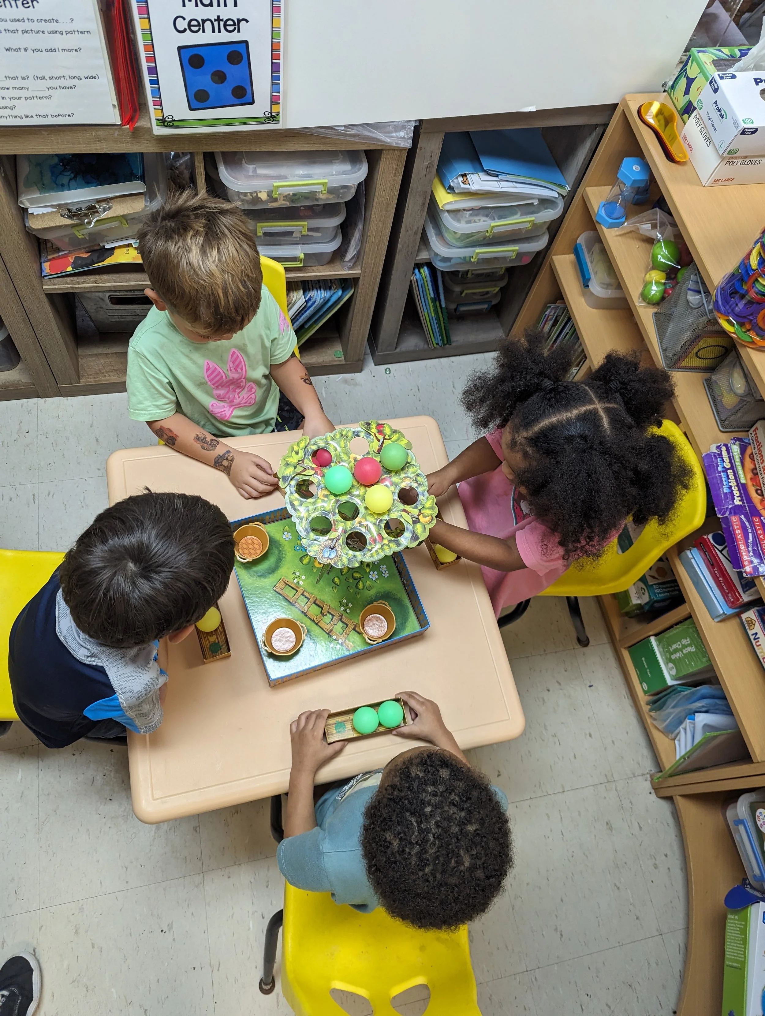 Children playing a game with colored balls and a tiered stand in a classroom.