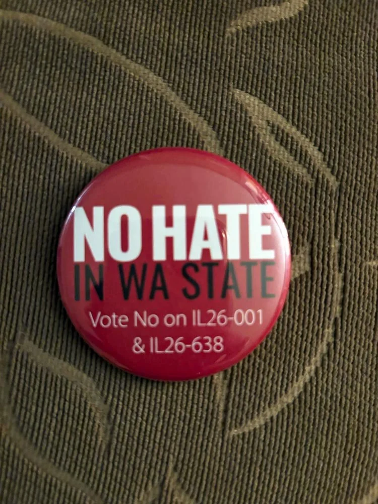 Red political campaign button with white and black text reading "NO HATE IN WA STATE" and additional voting information for measures IL26-001 and IL26-638.